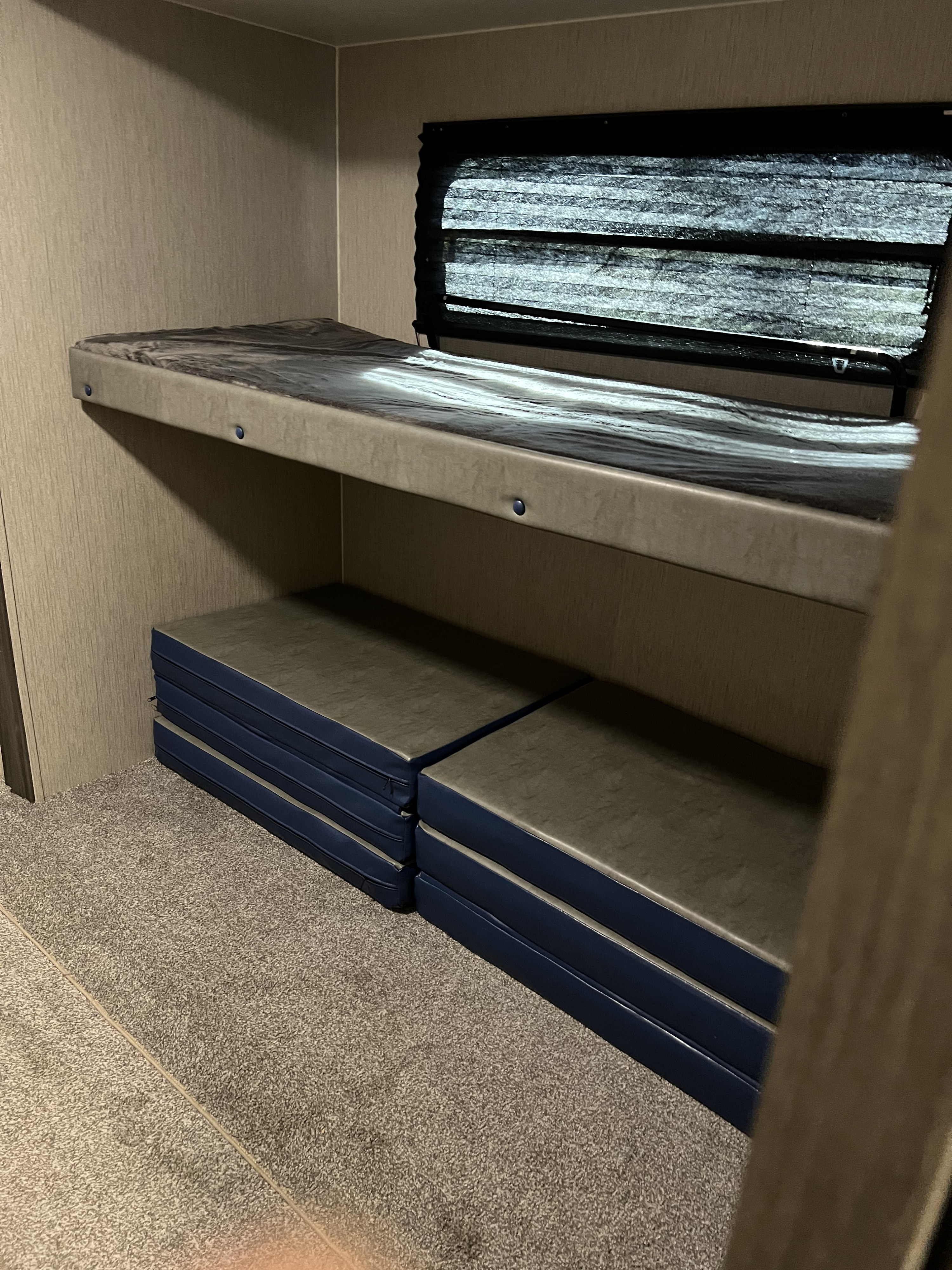 RV rental interior featuring an upper bunk bed with a window and folded sleeping mats on the carpeted floor.. Coachmen Freedom express 2020