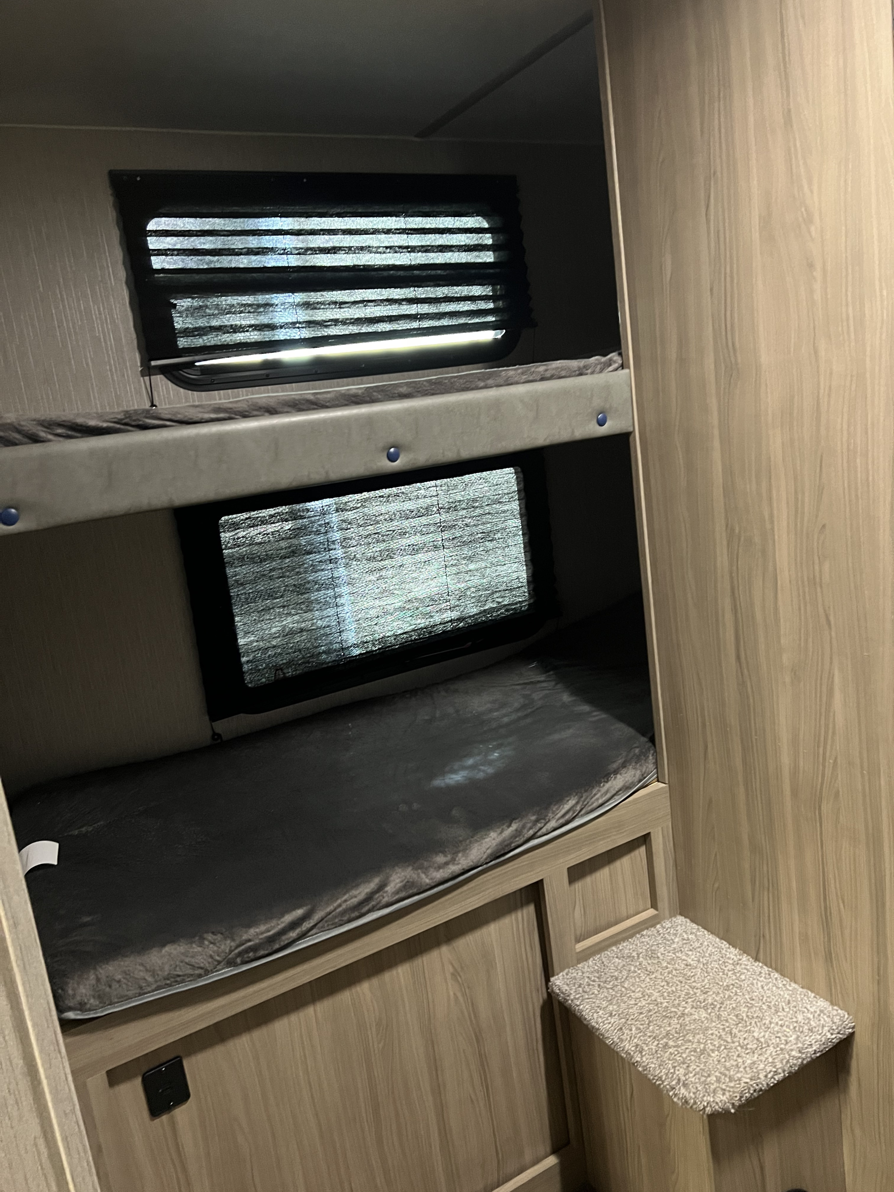 RV rental's bunk beds: Two sleeping areas with dark mattresses and windows, framed by light wood interior, plus a carpeted step.. Coachmen Freedom express 2020