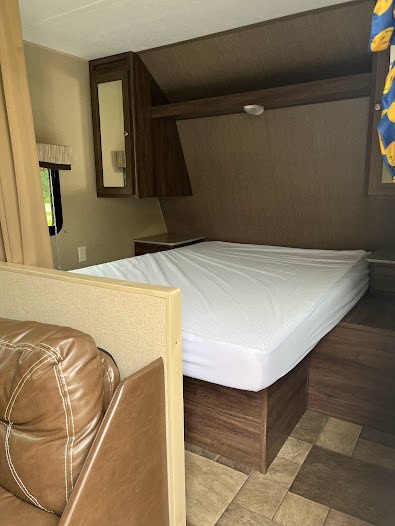 A well-appointed RV rental interior showing a comfortable bedroom with bed, overhead cabinets, and adjacent seating.. Dutchmen Coleman Lantern 2015