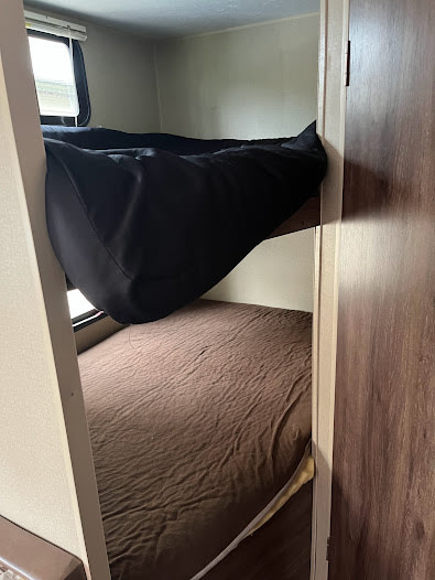 Cozy RV rental bunk beds: The top bed has a black comforter, the lower bed a brown sheet, ready for travelers.. Dutchmen Coleman Lantern 2015