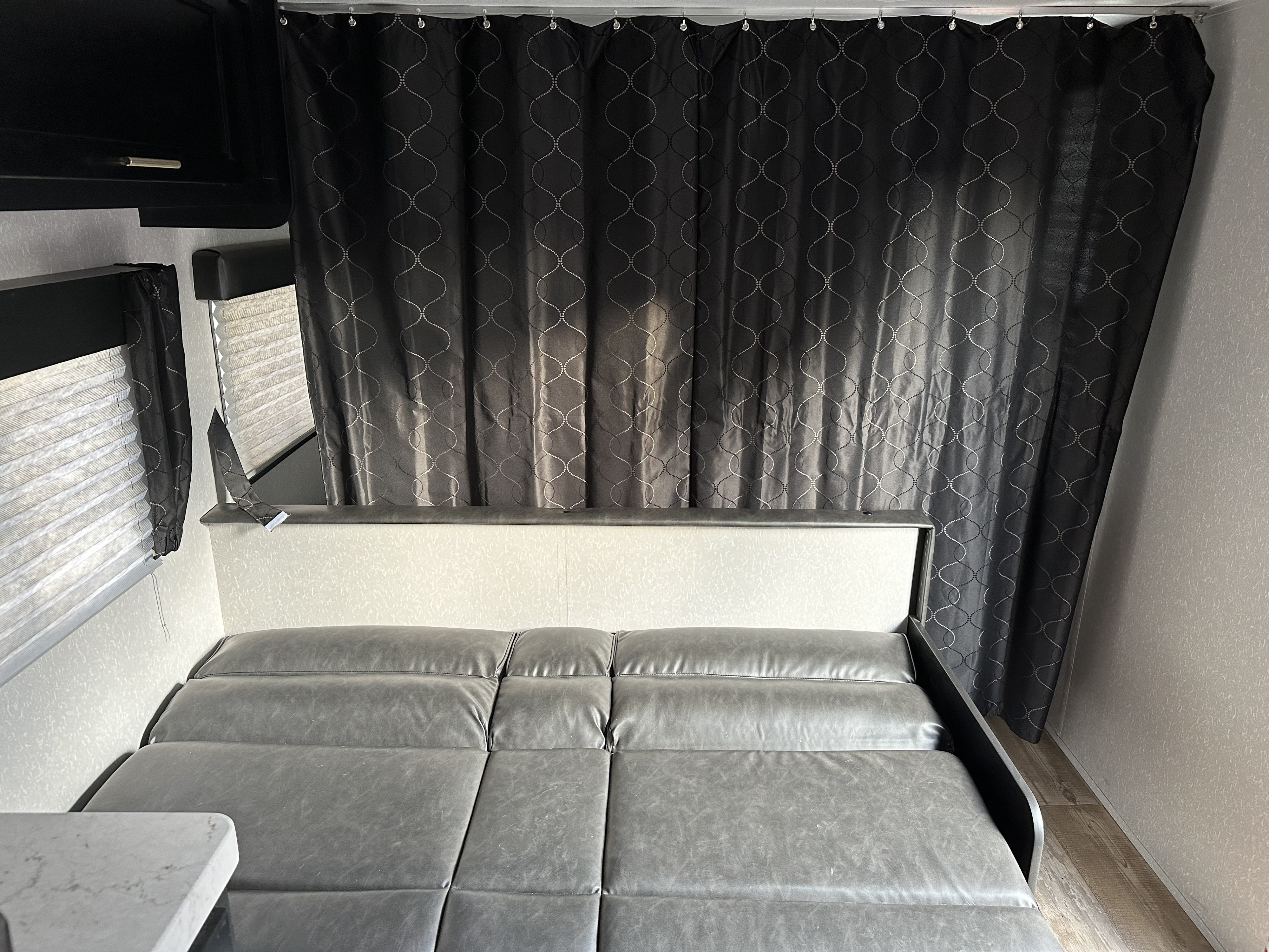 RV rental interior with dark patterned privacy curtains, pleated window blinds, and a grey convertible bed/seating area.. Forest River Cherokee Grey Wolf Special Edition 2022