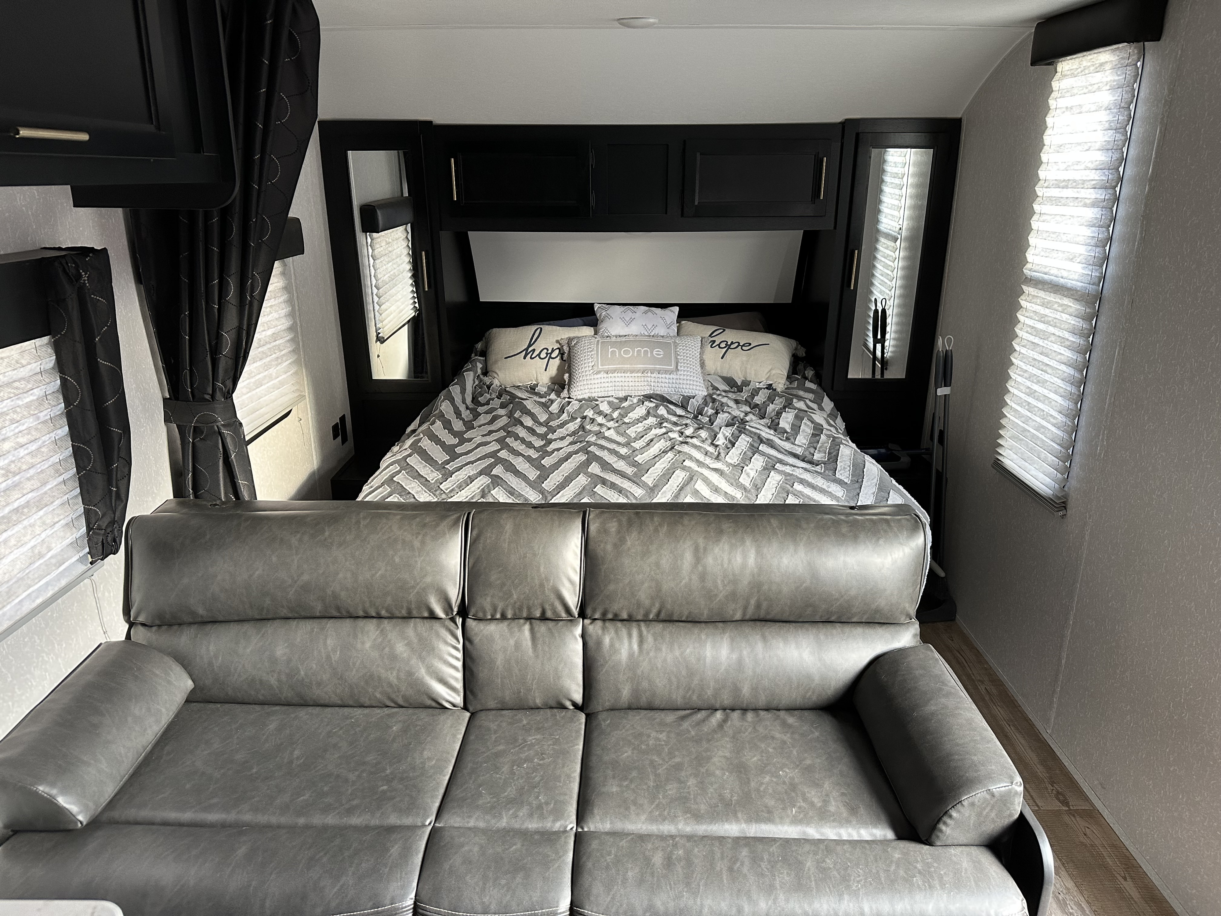 Comfortable RV rental interior: gray leather sofa, cozy bed with decorative pillows, and sleek overhead storage. Perfect for travel.. Forest River Cherokee Grey Wolf Special Edition 2022