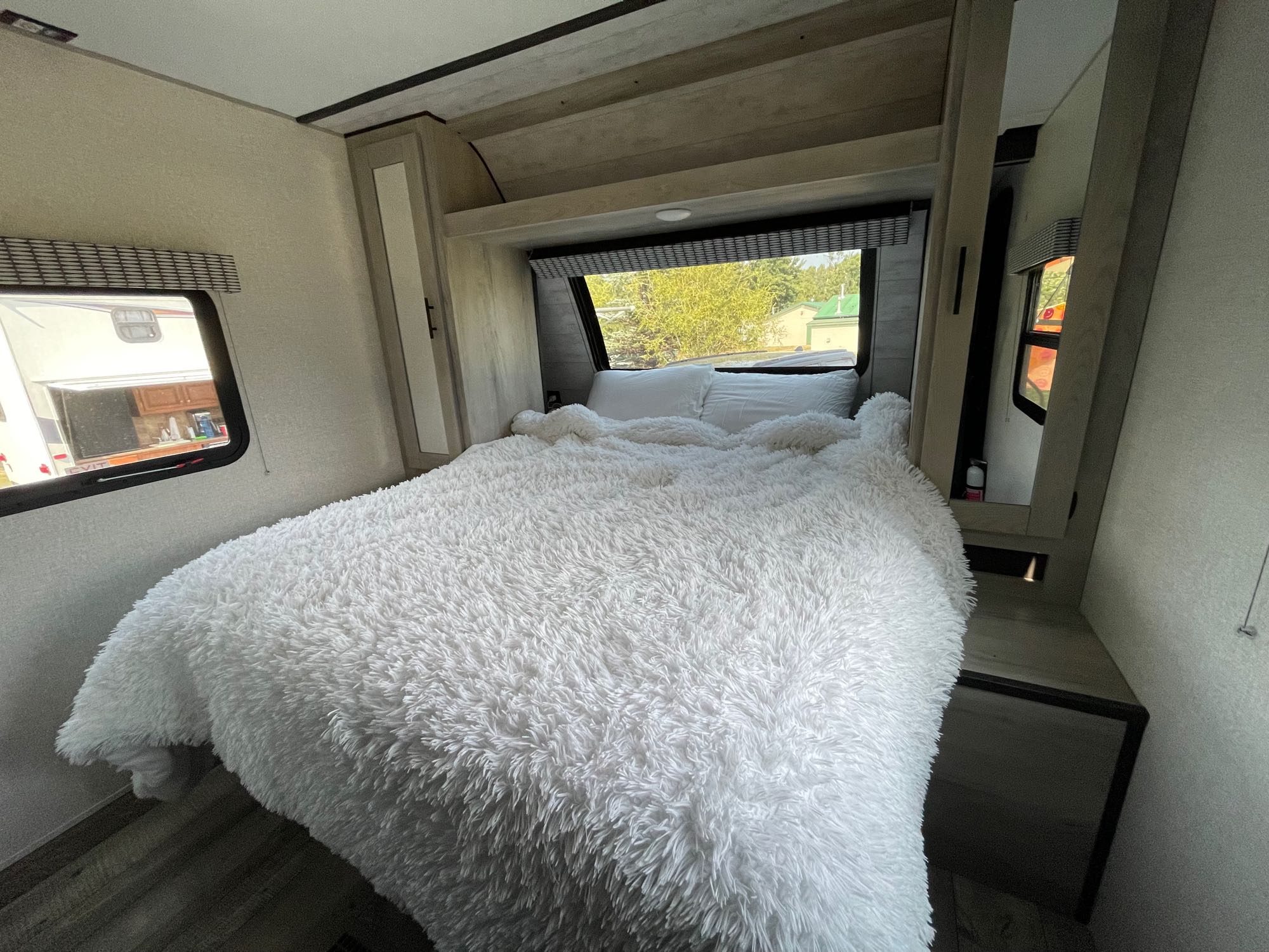 Spacious RV rental bedroom featuring a plush white bed, light wood interior, and large windows with outdoor views.. Connect SE 2022