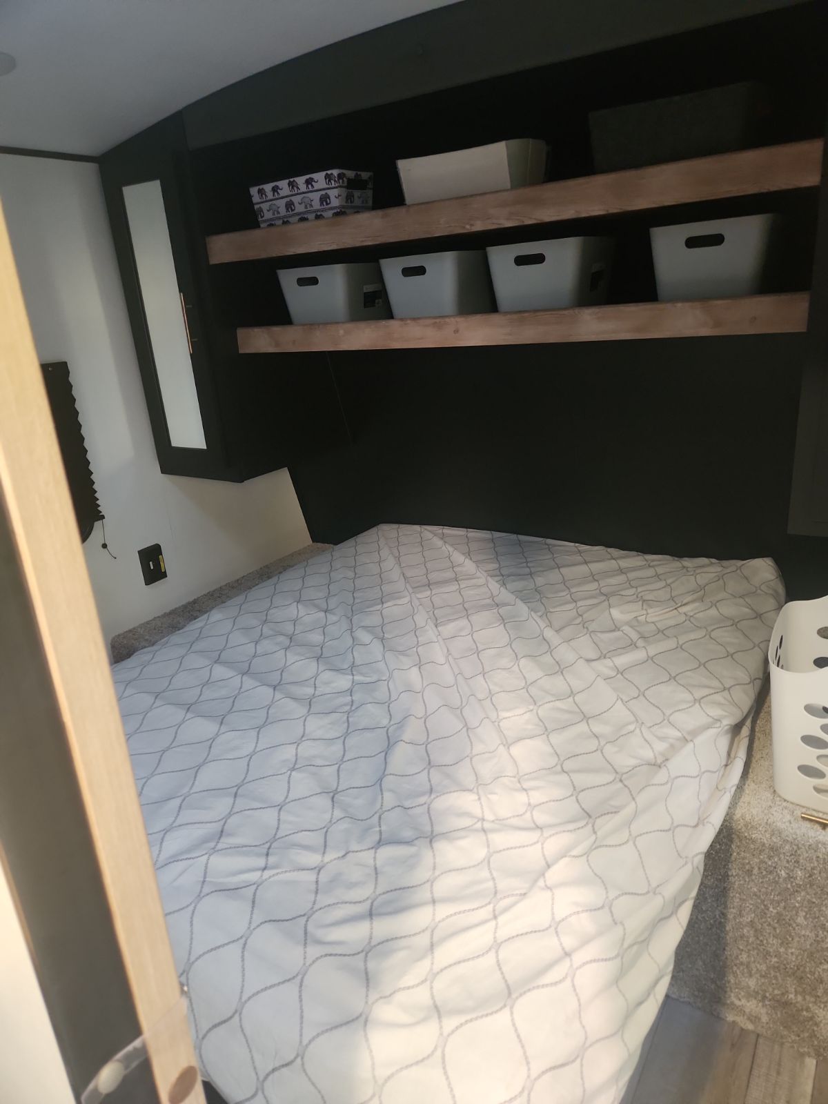 RV rental bedroom: A cozy bed with patterned cover & practical overhead storage shelves, perfect for your trips.. Keystone RV Springdale 2022