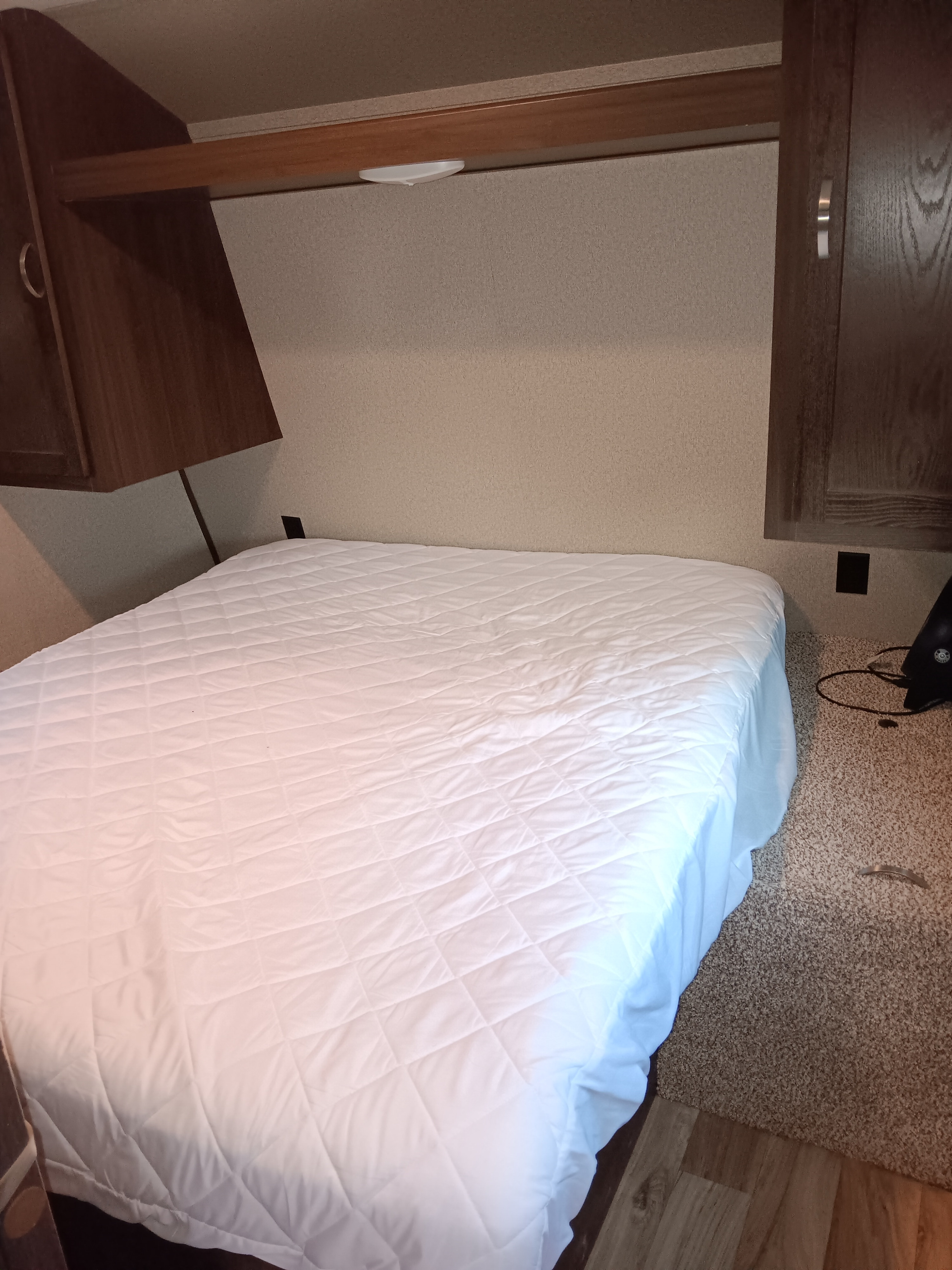 Cozy RV rental bedroom, featuring a comfortable bed with a white quilted mattress, overhead storage cabinets, and task lighting, perfect for travel.. Keystone Springdale 2019