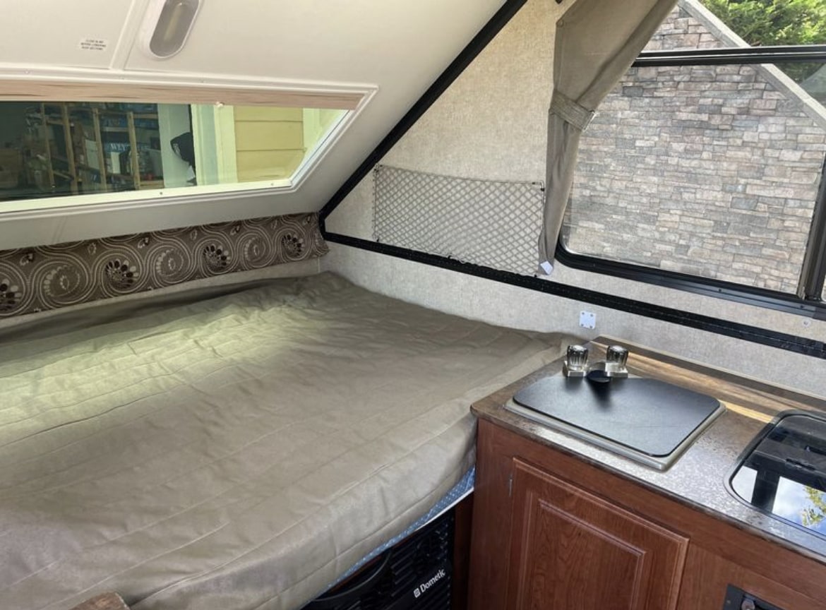 Inside a compact RV rental, showing a bed with tan cover and a small kitchen counter.. Forest River Rockwood Premier 2015