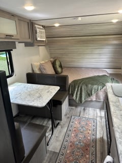 Cozy RV rental interior featuring a practical dinette, comfy bed/lounge area with pillows, and compact kitchen counter.. Dutchmen Coleman Lantern LT 2023