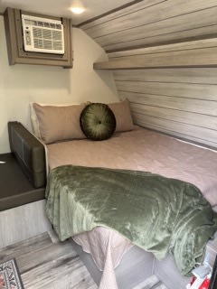 Cozy RV rental bedroom with a comfortable bed, green accents, and wall-mounted AC unit, perfect for your travel comfort.. Dutchmen Coleman Lantern LT 2023