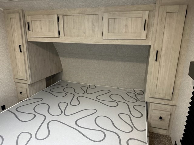 Inside an RV rental: a cozy bedroom featuring a patterned mattress, overhead storage, and side cabinets for your travels.. Forest River East to West Silverlake 2022