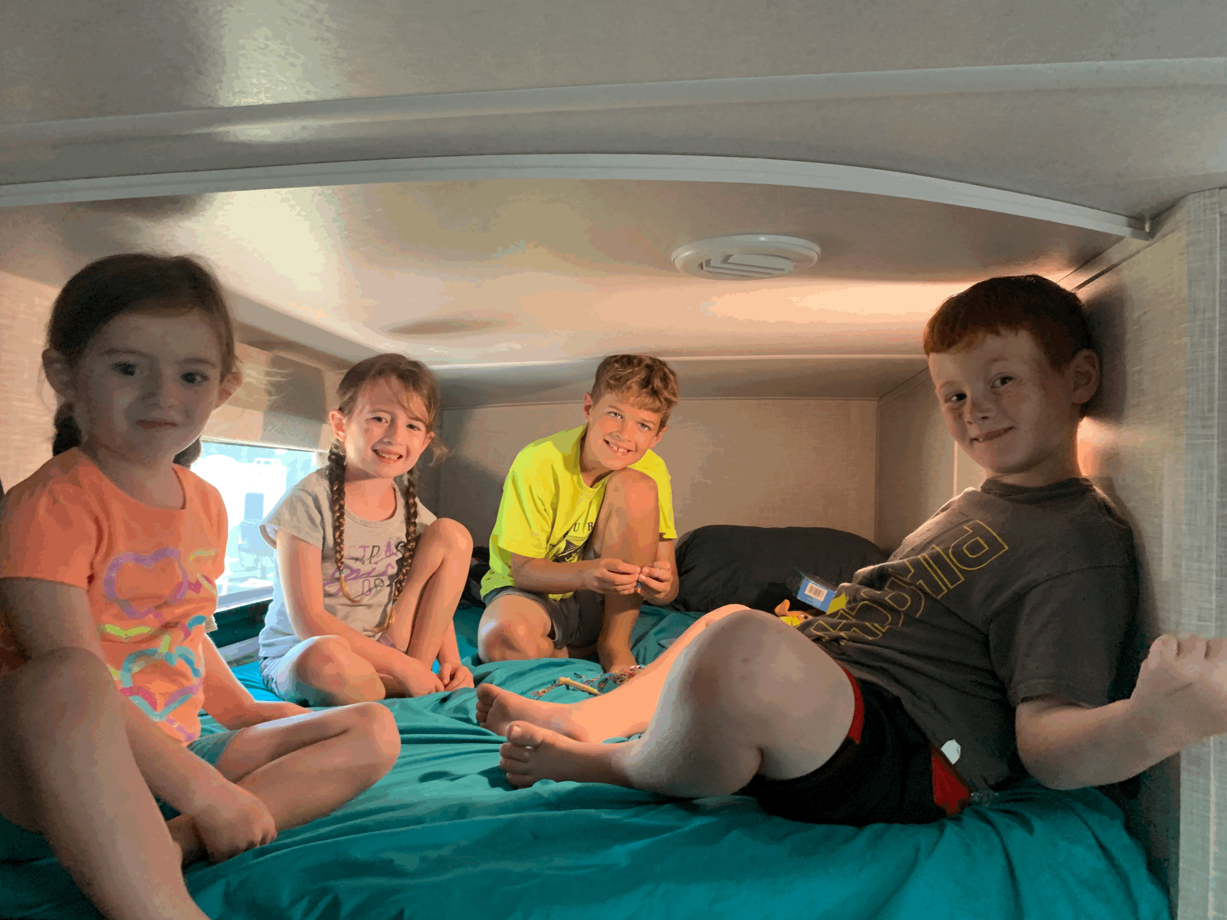 Four children smiling on a teal bed inside an RV rental. Cozy family travel fun!. Forest River Flagstaff Super Lite 2023