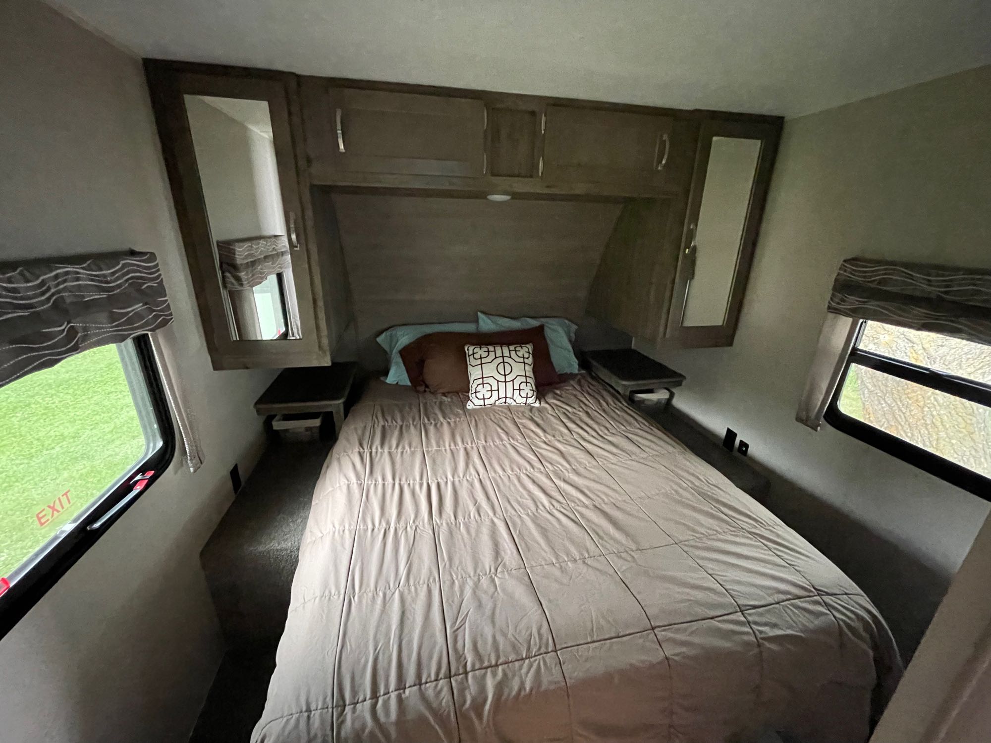 Inside an RV rental: a comfortable bedroom with a queen-sized bed, mirrored cabinets, and emergency exit windows.. Forest River Puma 2019