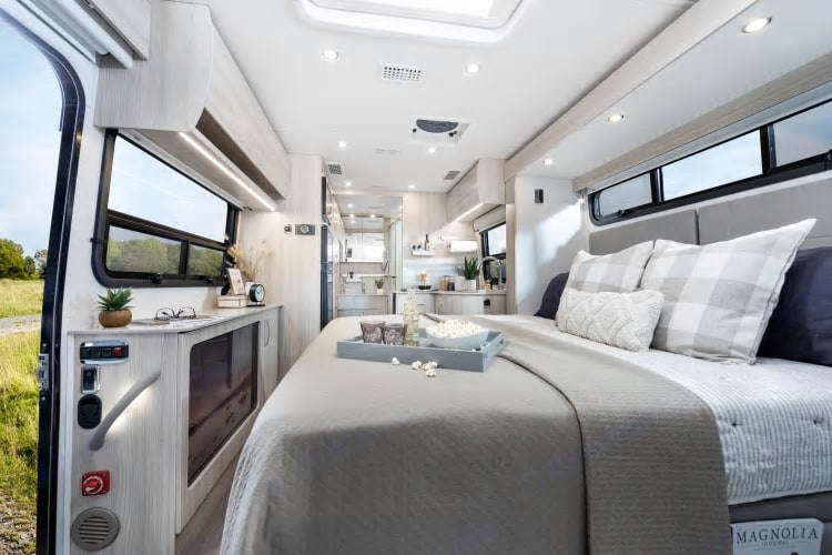 Bright, spacious RV rental interior: a comfy bedroom with snacks leads to a modern living and kitchen area.. Leisure Travel Vans Unity 2022