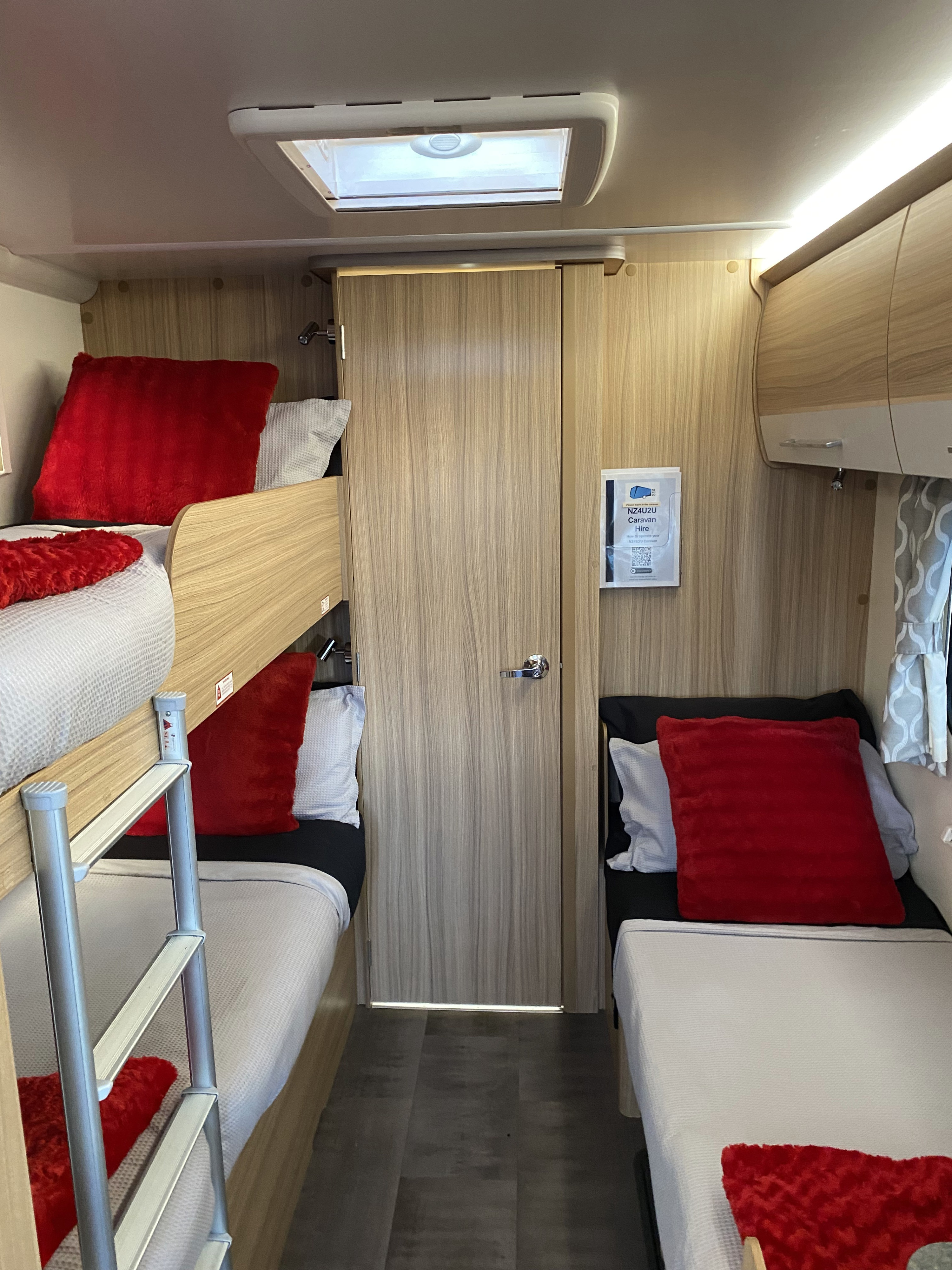 Cozy RV rental interior showing bunk beds (left) with red cushions, a single bed (right), and a central door. Ideal for family travel.. Bailey x 2022