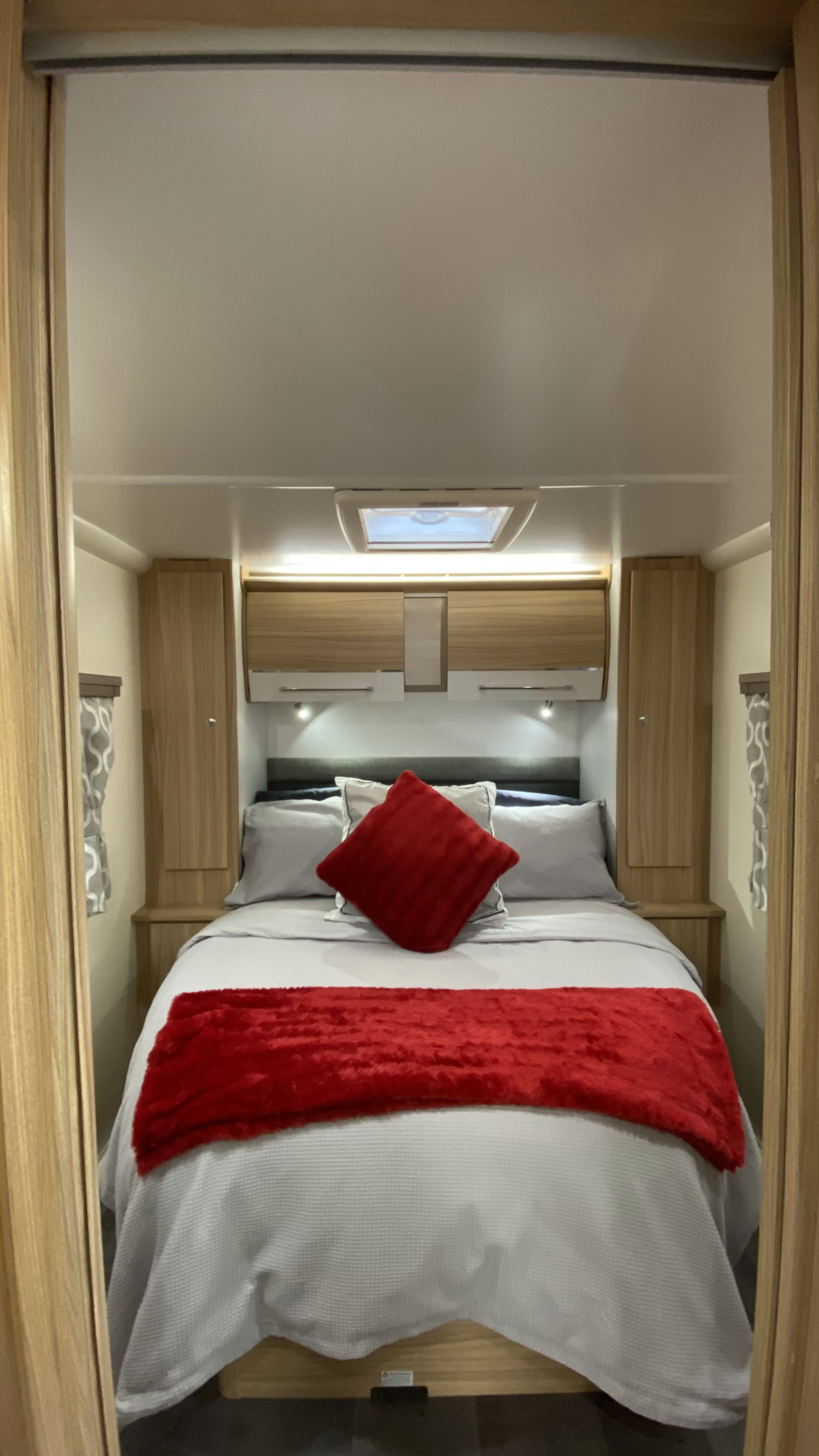 This compact RV rental bedroom offers a comfortable bed with grey linens & red accents, plus overhead storage.. Bailey Pheonix 640 2022