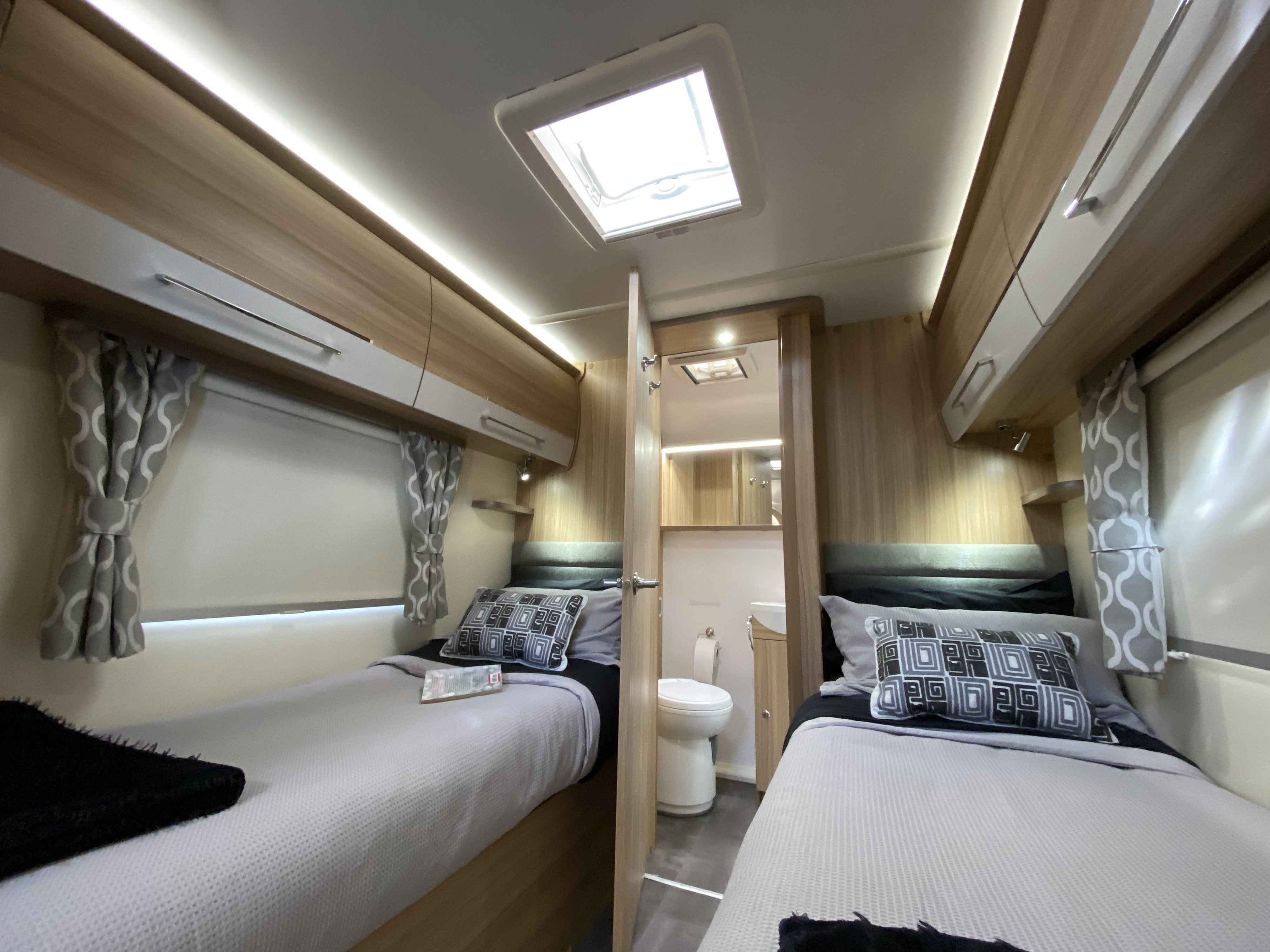 Bright RV rental interior: Twin beds, overhead storage, ambient lighting, and a compact bathroom. Perfect for comfortable journeys.. Bailey x 2022