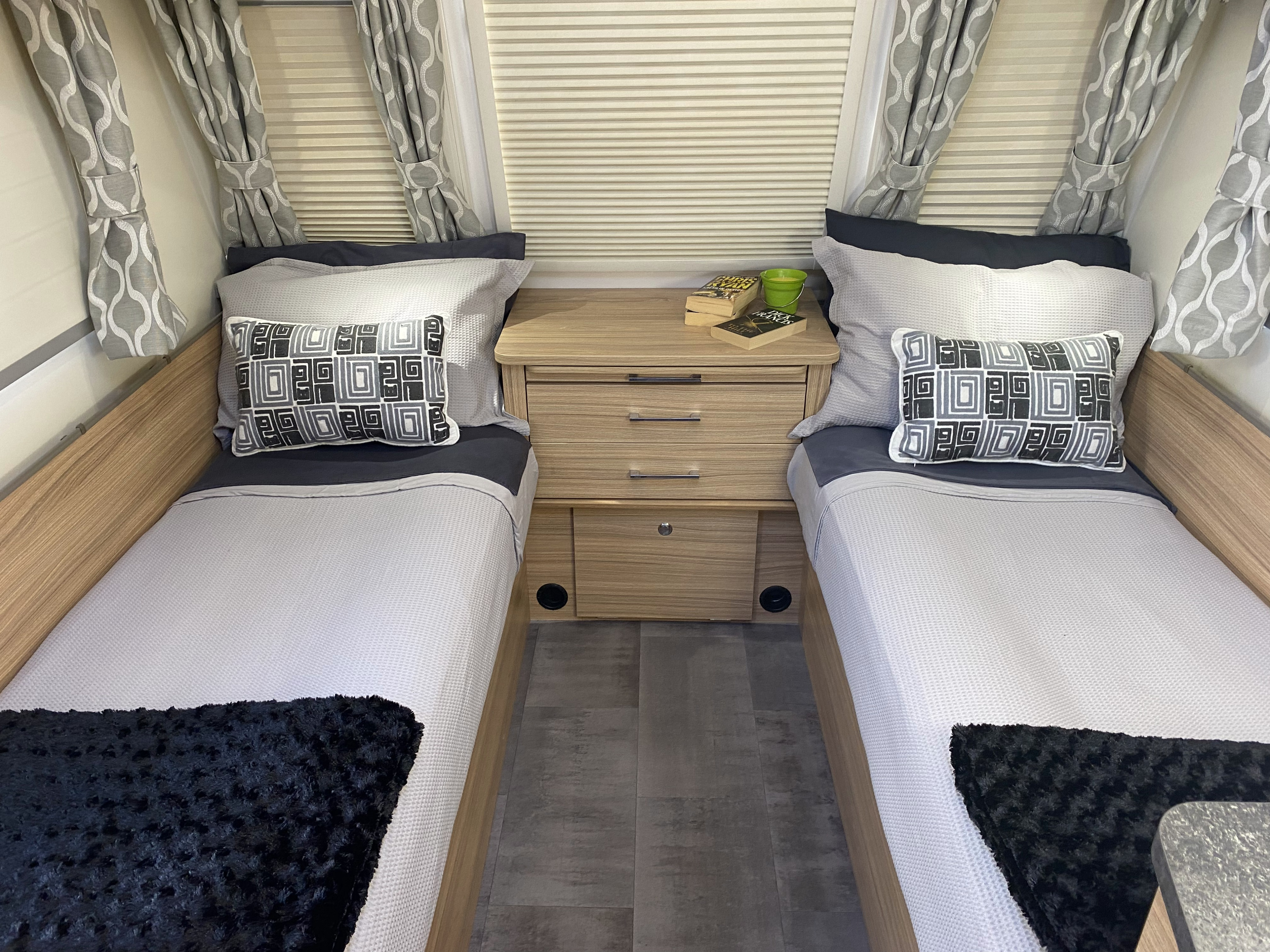 Cozy RV rental twin bedroom featuring two beds, nightstand, patterned curtains, and inviting bedding for a compact stay.. Bailey x 2022