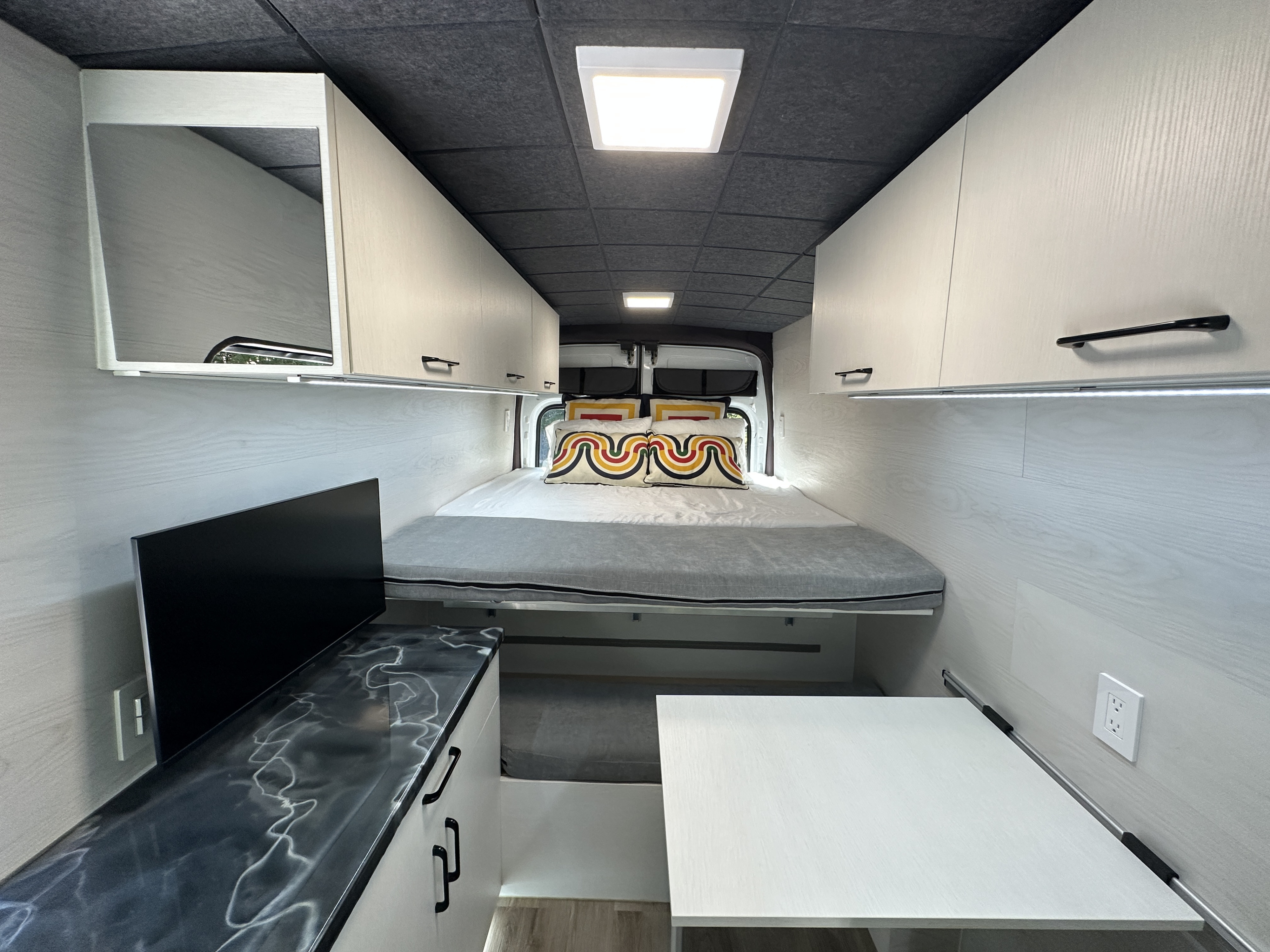 Sleek rv rental camper van interior featuring a comfortable bed, cabinets, kitchenette, and dining.. Ford Transit T-350 2020