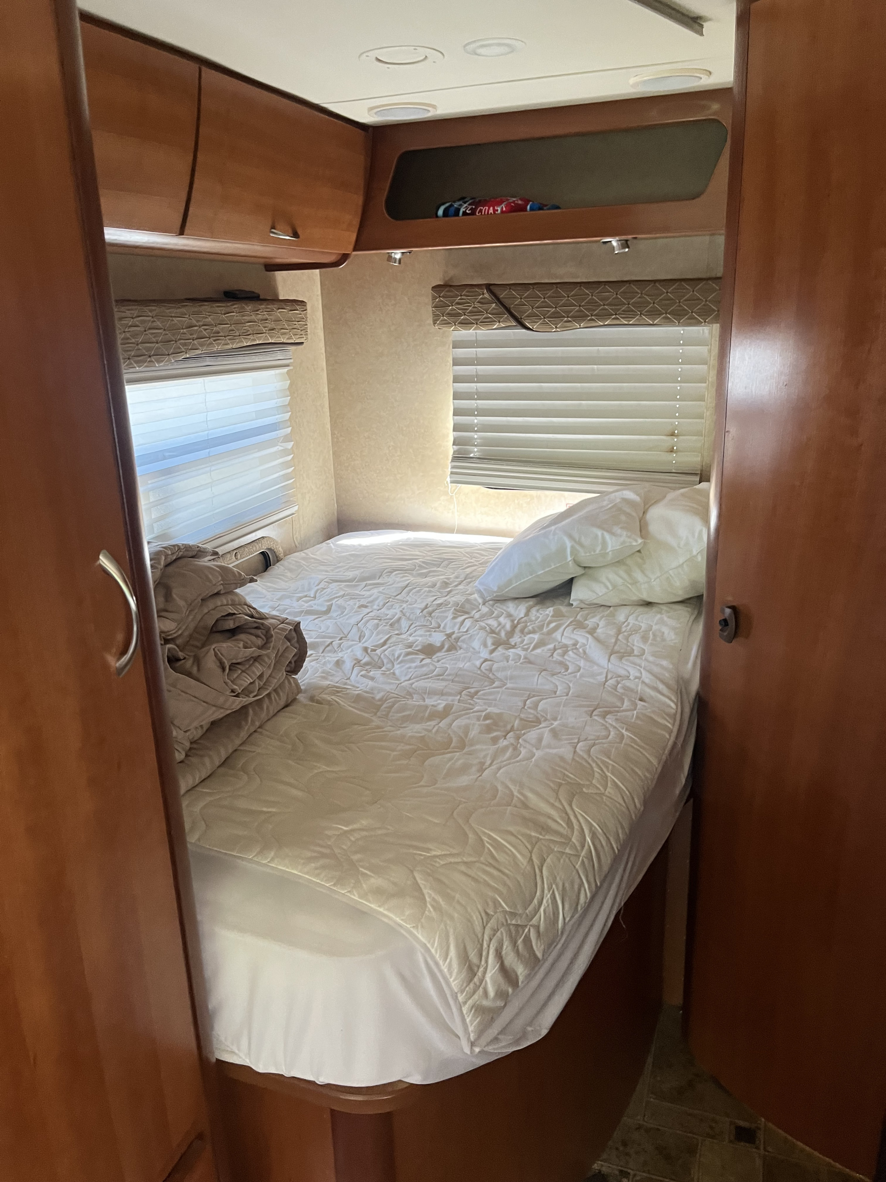 Step inside an RV rental: a compact bedroom with a comfortable bed, windows, and overhead storage cabinets.. Monaco Covina 2009