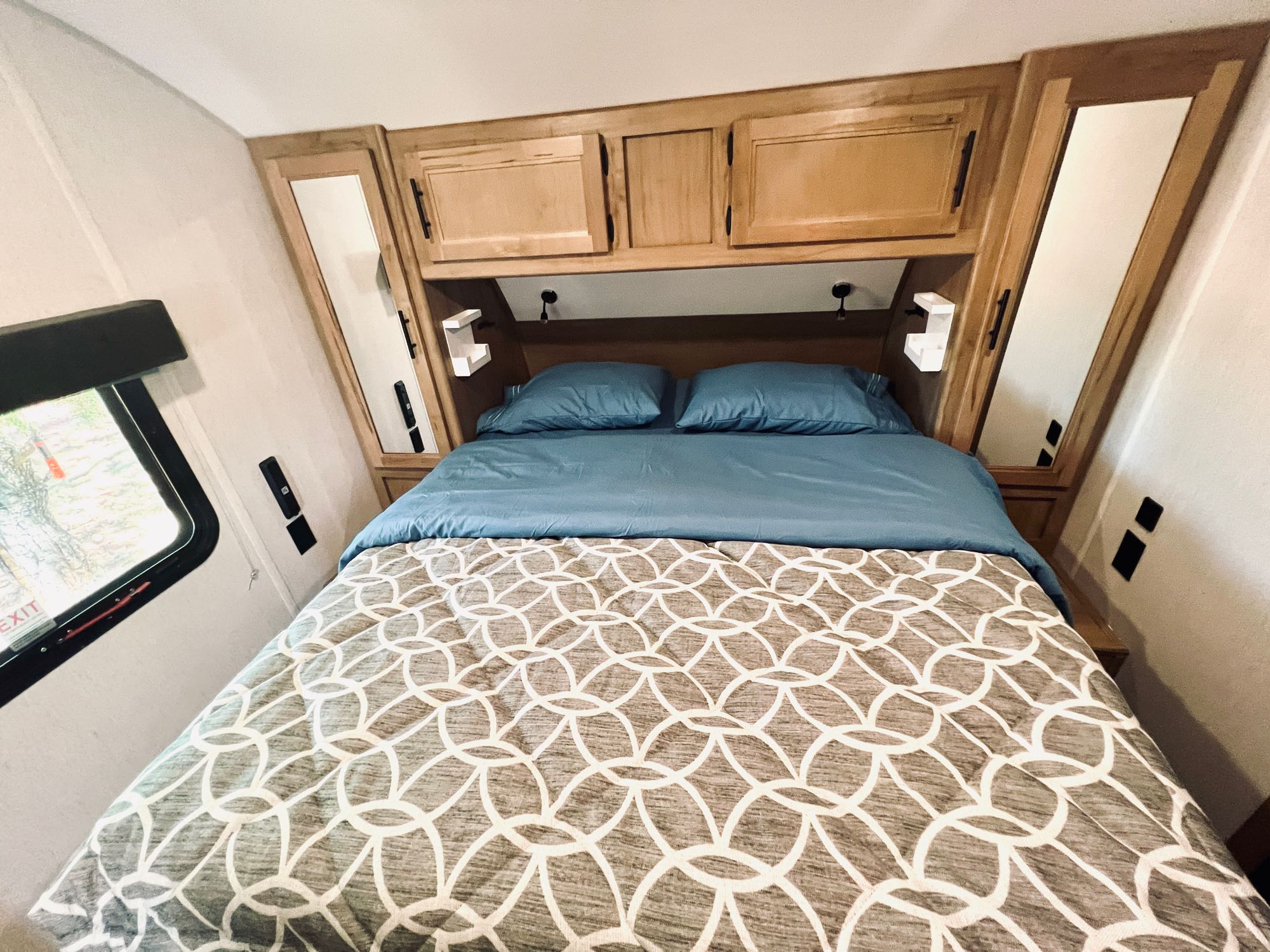 Cozy RV rental bedroom: blue bed, patterned comforter, overhead storage cabinets, and side mirrors.. Forest River Cherokee Grey Wolf 2023