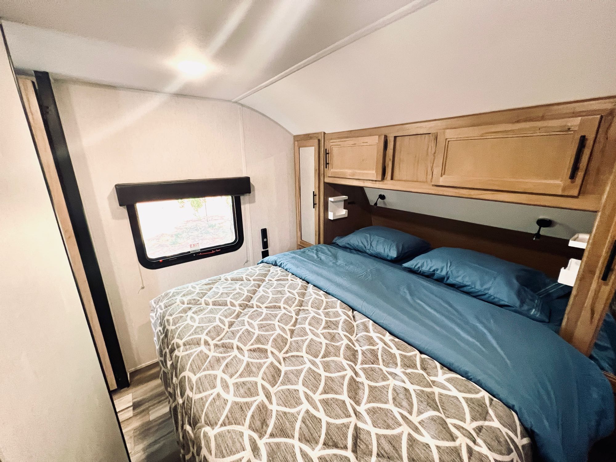 Cozy RV rental bedroom with patterned comforter, blue bedding, and overhead cabinets, ideal for your next adventure.. Forest River Cherokee Grey Wolf 2023