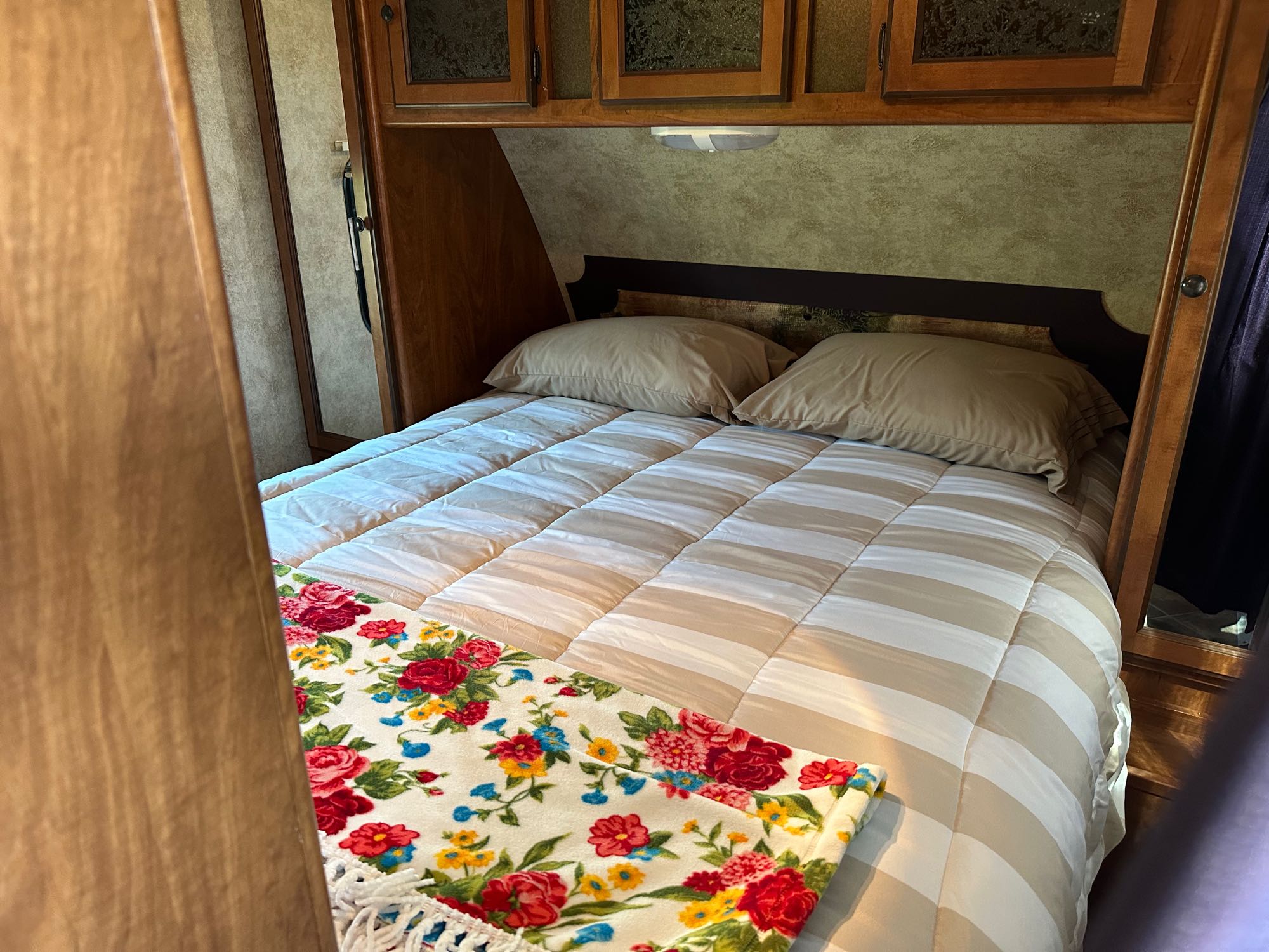 Inside a comfortable RV rental: A cozy bedroom with striped comforter, tan pillows, and a vibrant floral blanket.. Keystone RV Passport Ultra Lite 2012