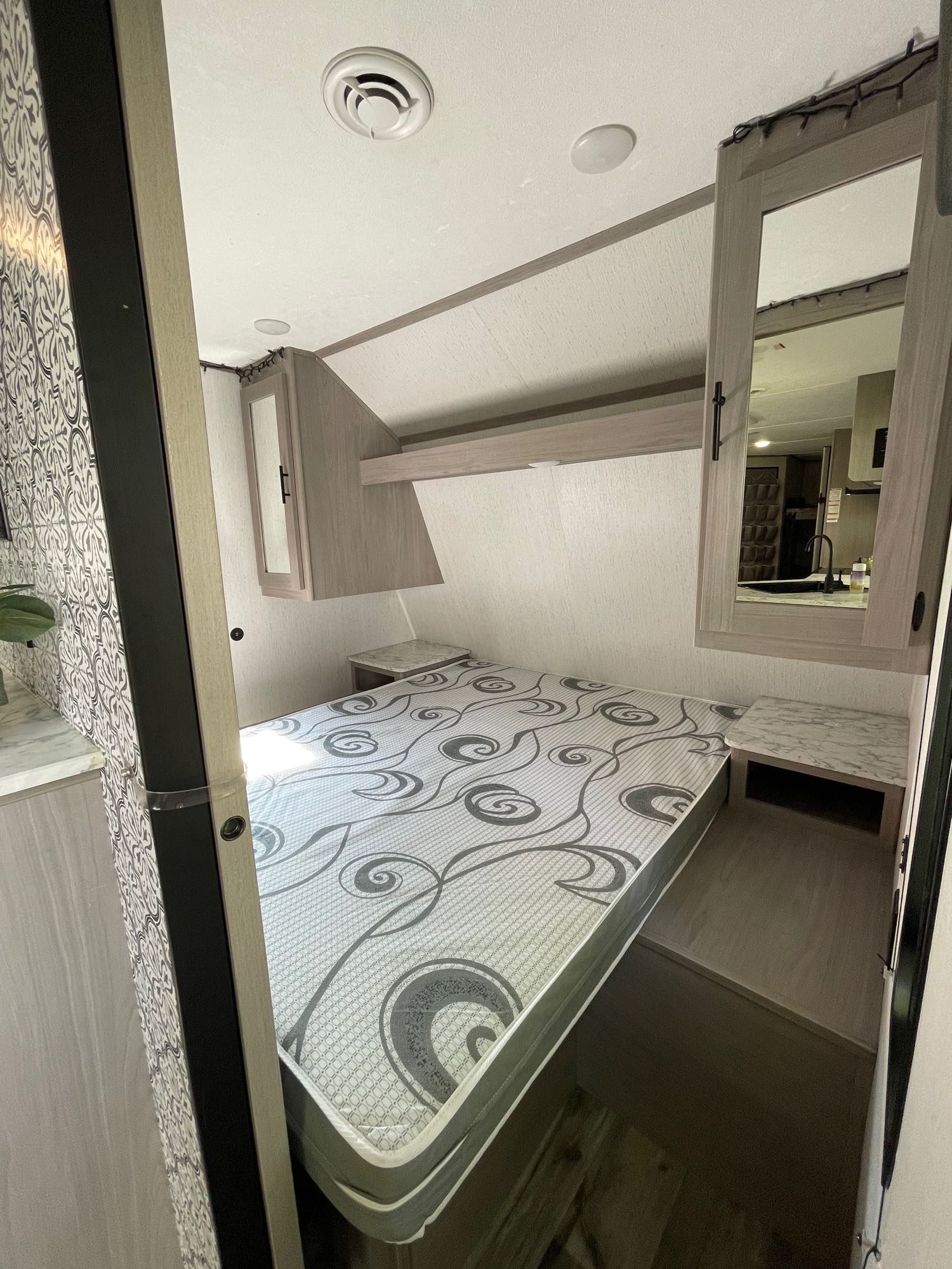Experience comfort in this RV rental bedroom. Features a patterned bed, compact storage, and mirrored cabinets.. Coleman 263BH 2022