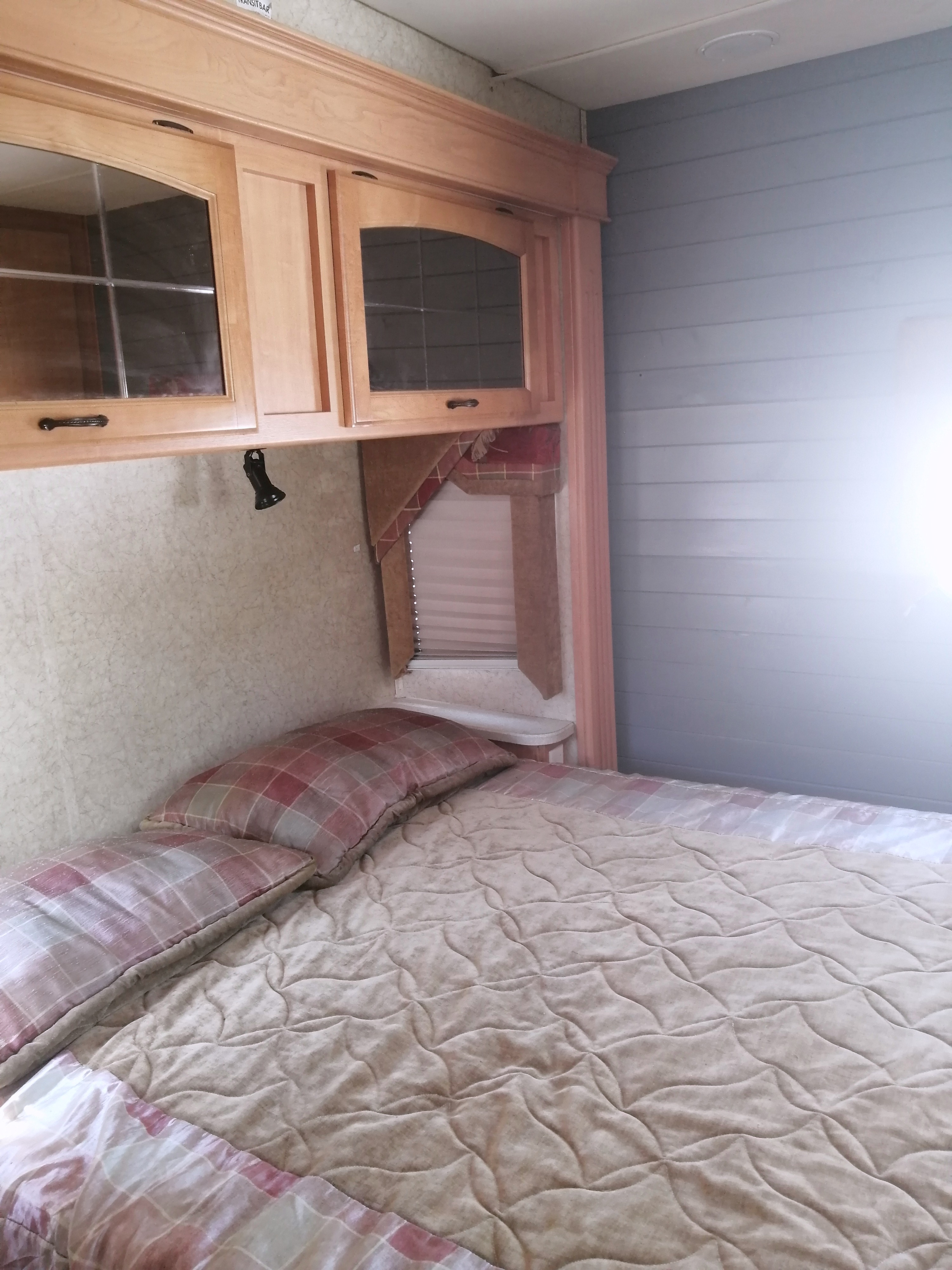 Cozy RV rental bedroom featuring a comfortable bed, overhead wooden cabinets, and modern blue paneled walls.. Jayco Greyhawk 2007