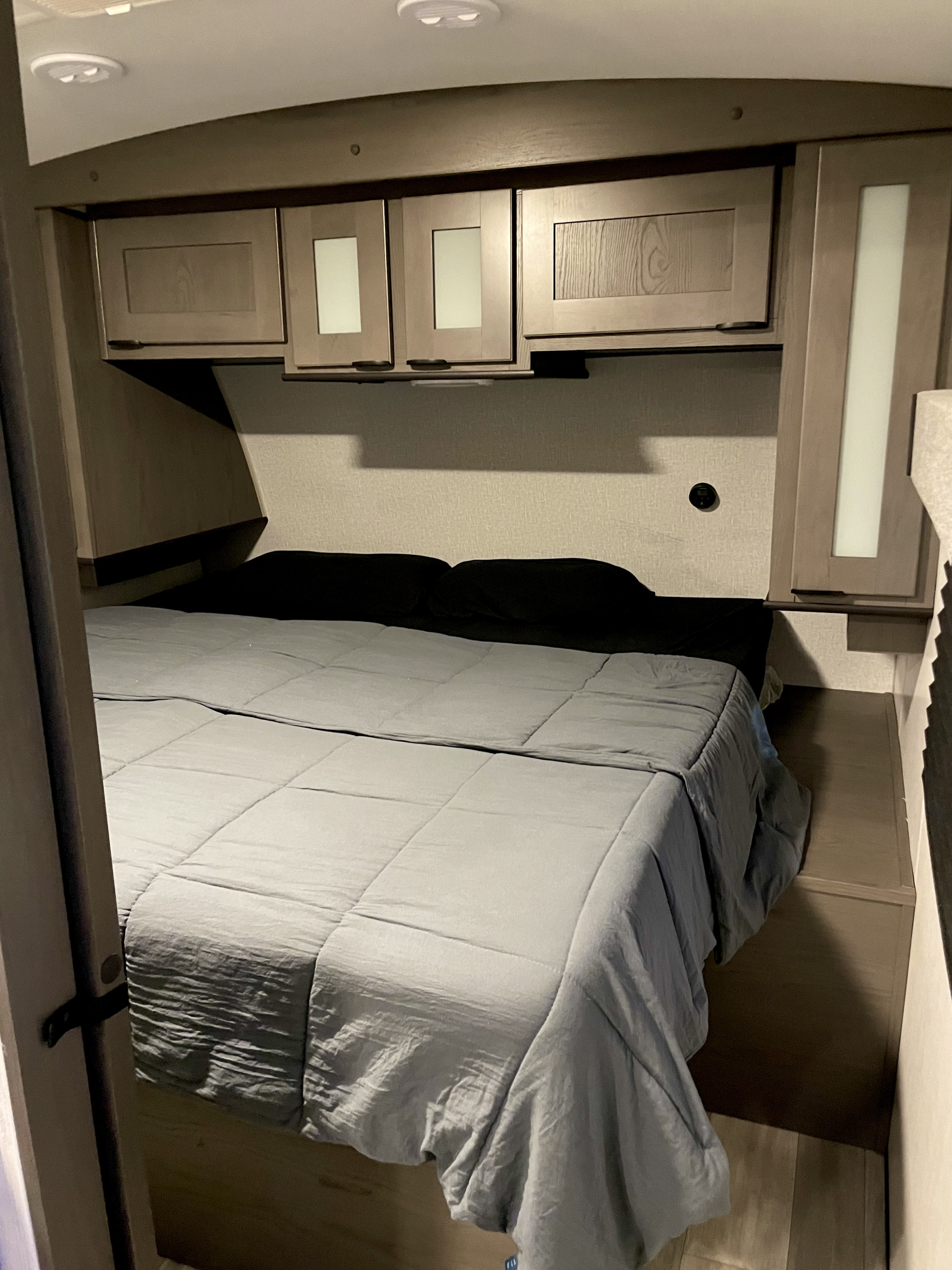 A cozy RV rental bedroom features a gray bed with black pillows, overhead storage cabinets, and soft lighting, ideal for travel.. Cruiser RV MPG Ultra Lite 2022