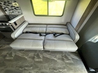 RV rental interior: A light-colored sofa bed with seatbelts extends into a sleeping area, next to a small kitchen counter.. Gulf Stream Conquest 63111 2024