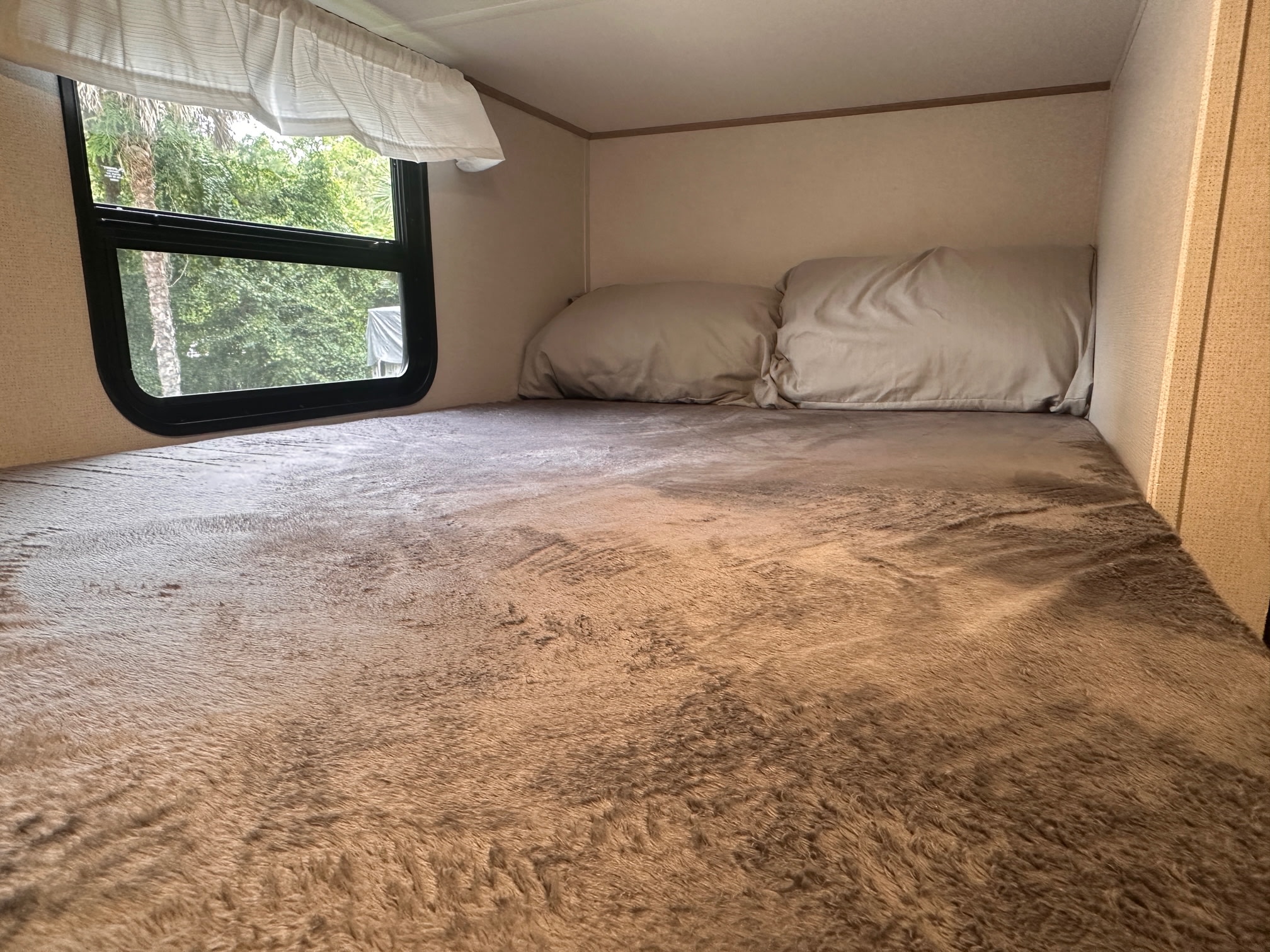 Cozy RV rental bunk bed featuring a plush, soft blanket, pillows, and a window looking out at green trees.. Forest River Avenger LE 2022