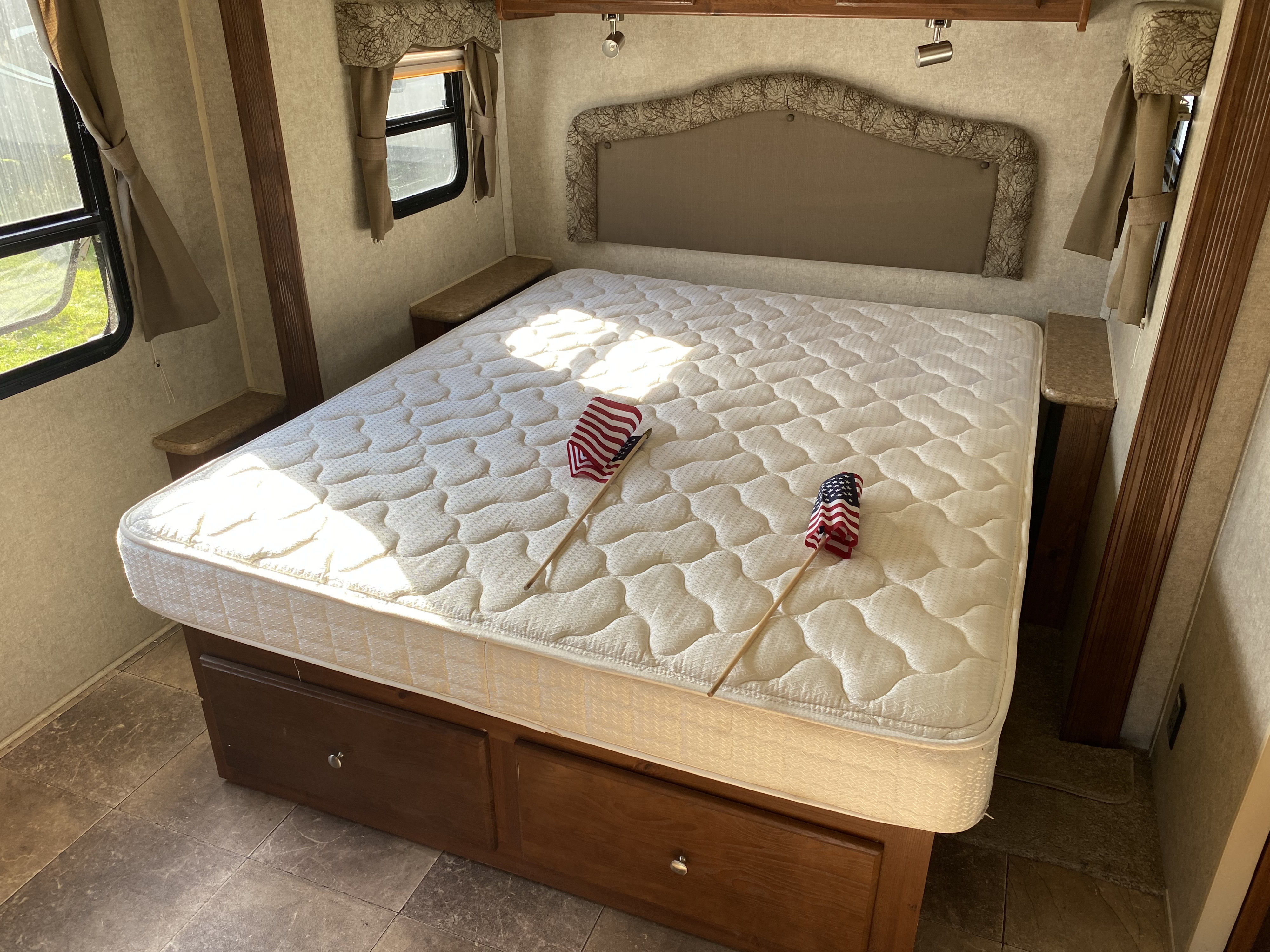 Cozy RV rental bedroom featuring a comfortable mattress, under-bed storage, windows, and small flags.. Forest River Rockwood Windjammer 2012
