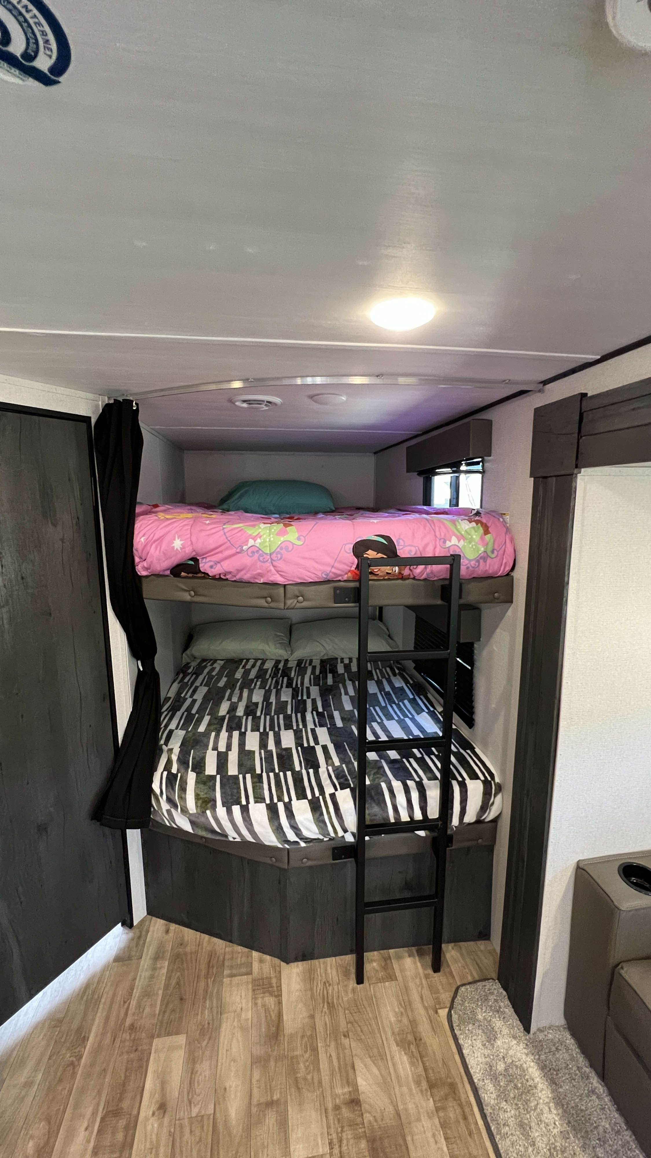 Cozy RV rental interior featuring bunk beds with a ladder, wood-look flooring, and soft bedding, perfect for family travel.. Keystone RV Hideout 2022