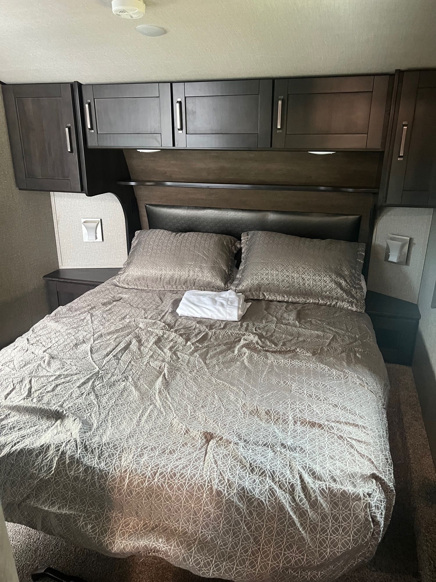 Inside an RV rental: a compact bedroom featuring a bed with patterned bedding, side tables, and ample storage.. Grand Design Reflection 2021