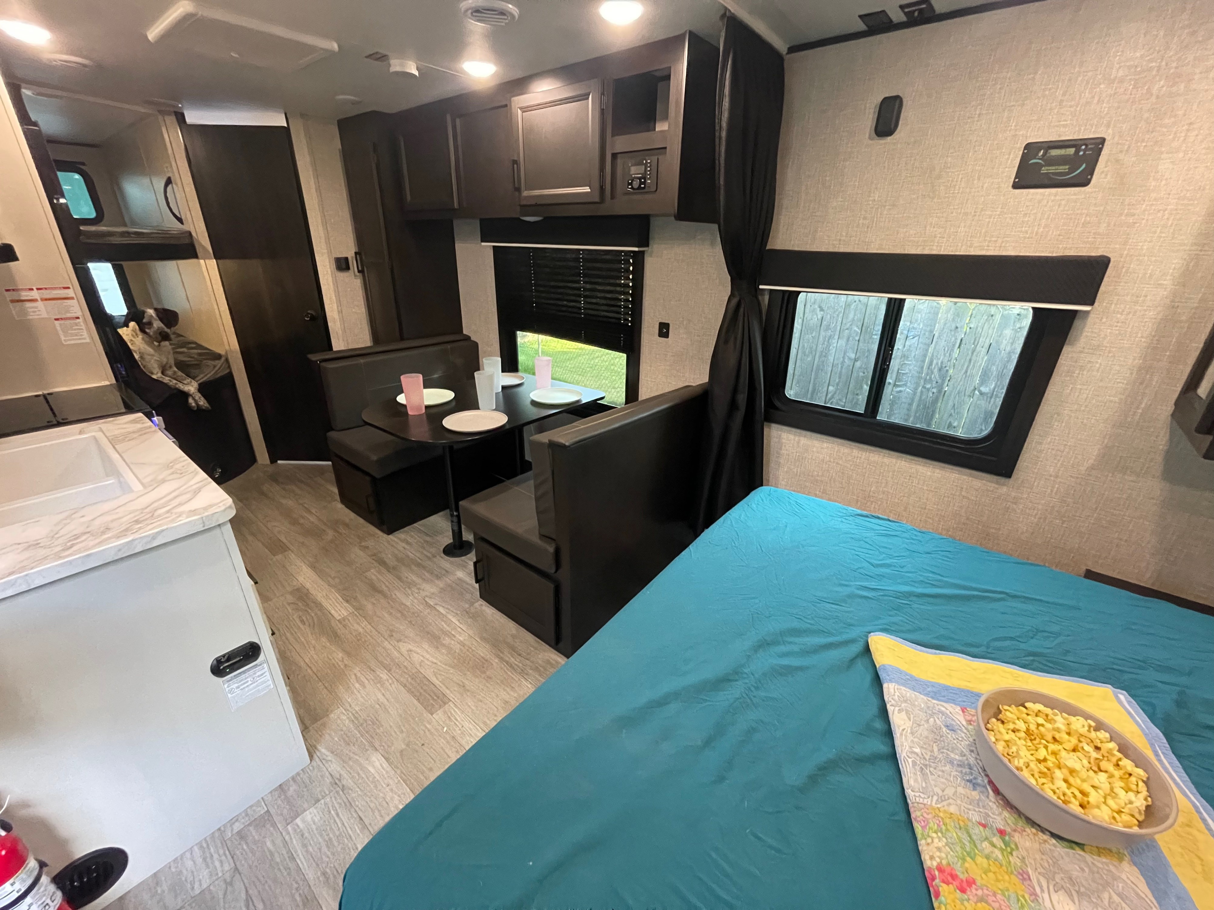 Inside a comfortable rv rental: bed with popcorn, dining booth, kitchen counter, and bunk beds with a sweet dog.. Jayco Jay Flight 2023