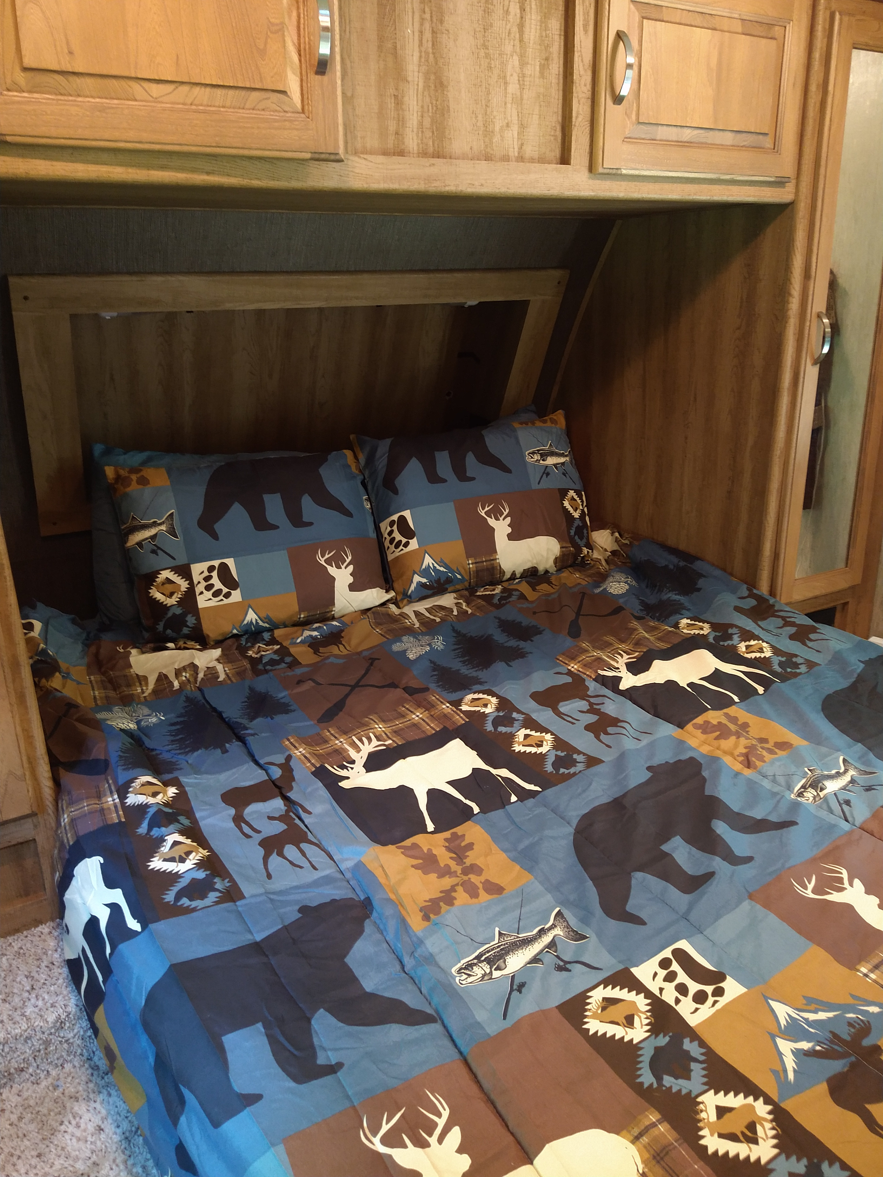 Comfortable RV rental bedroom featuring wood-paneled walls & nature-themed bedding with bears, deer, and fish for a rustic feel.. Keystone RV Laredo 2015