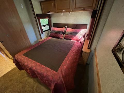 Cozy RV rental bedroom featuring a large bed with a red comforter, overhead cabinets, and a side window.. Itasca Sunrise 2008