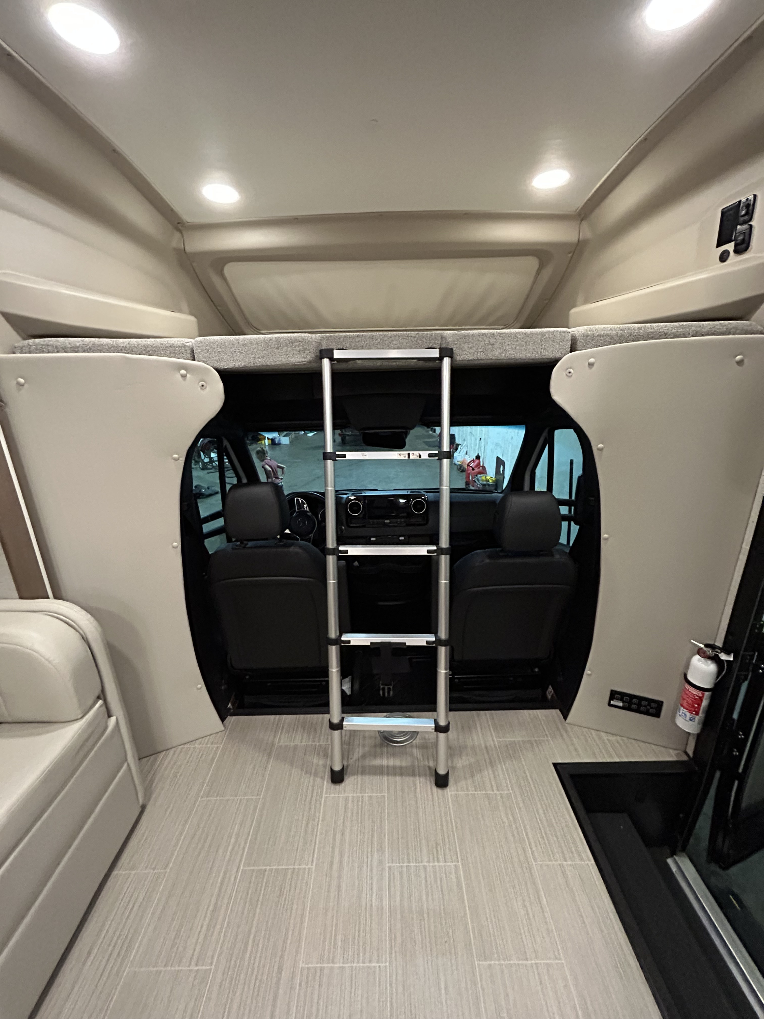 Inside an RV rental, featuring a cozy over-cab sleeping area with an access ladder, light-colored flooring, and front cabin view.. Jayco Melbourne 2022