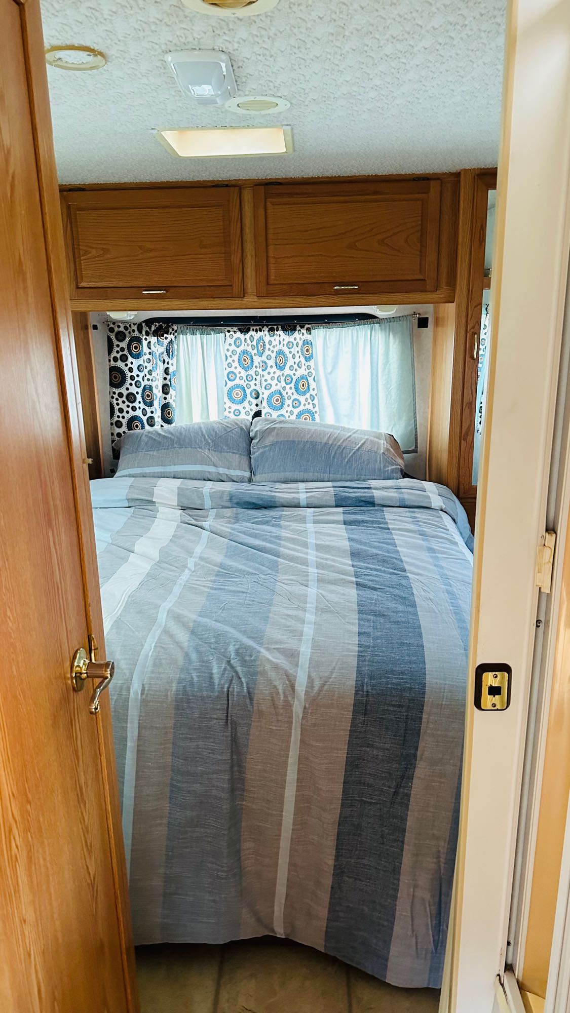 Step into comfort: a cozy RV rental bedroom featuring a striped bed and overhead storage.. Itasca Spirit 2001
