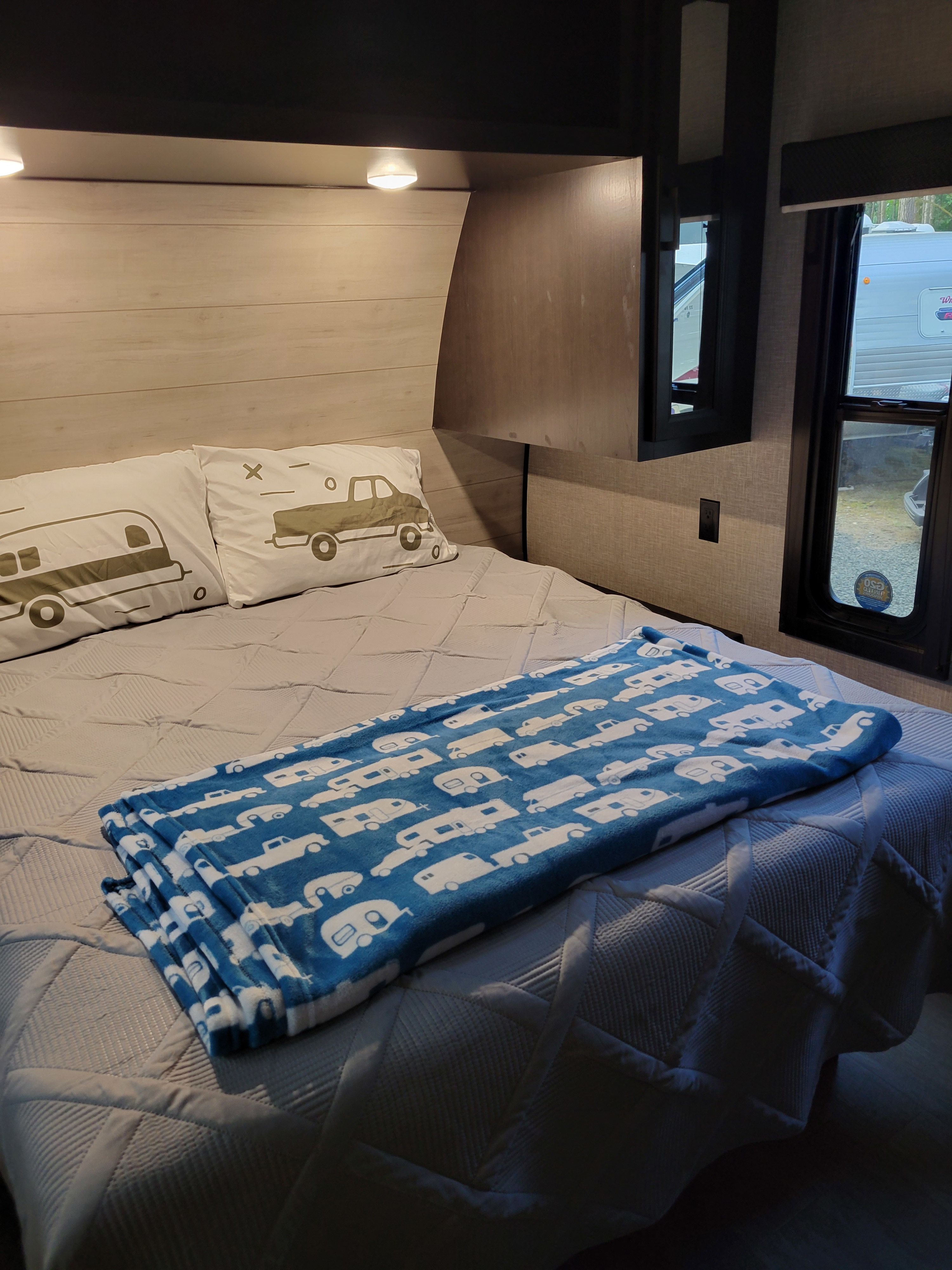 Cozy RV rental bedroom with a bed, camper-themed pillows, and a blue blanket. An RV is visible outside the window.. Jayco Jay Flight Baja Edition 2023