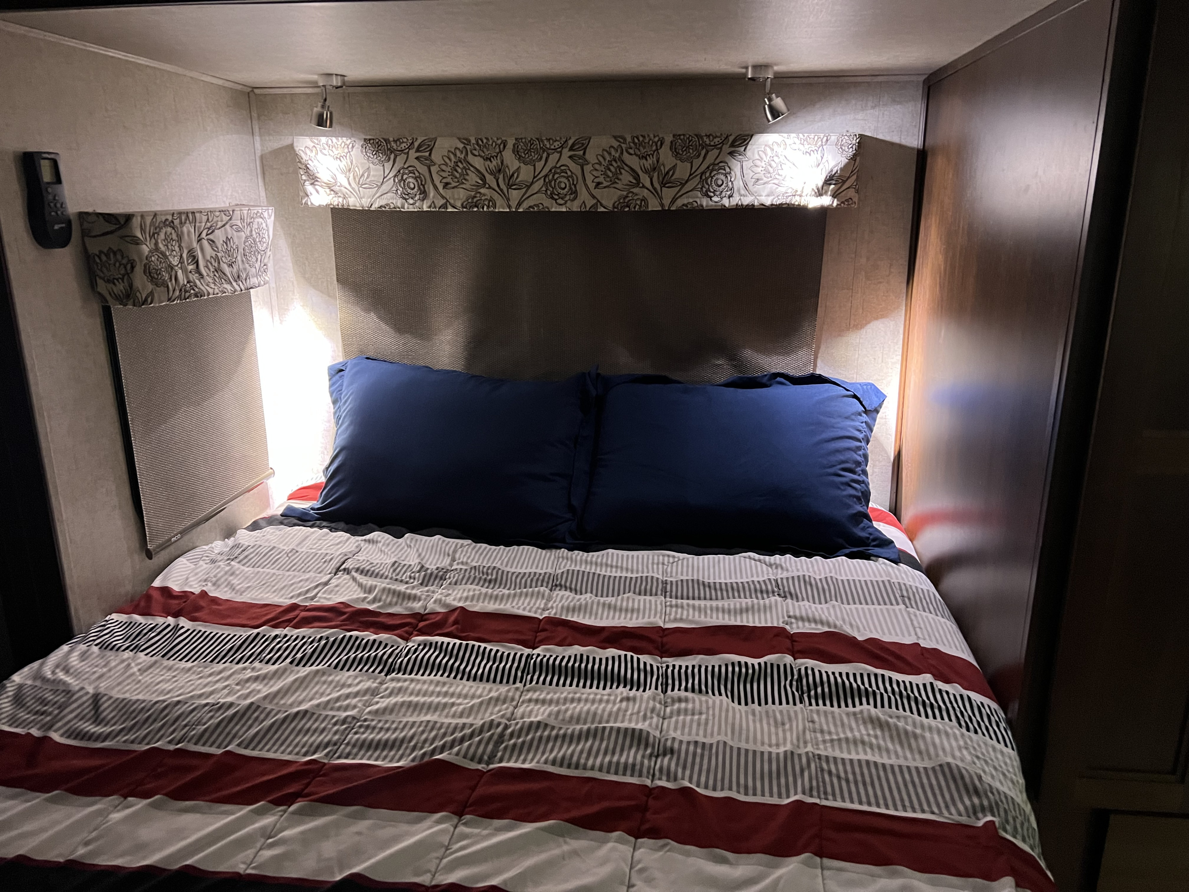 RV rental bedroom interior: bed with striped comforter, blue pillows, side lights, and window shade visible.. Forester MBS 2018