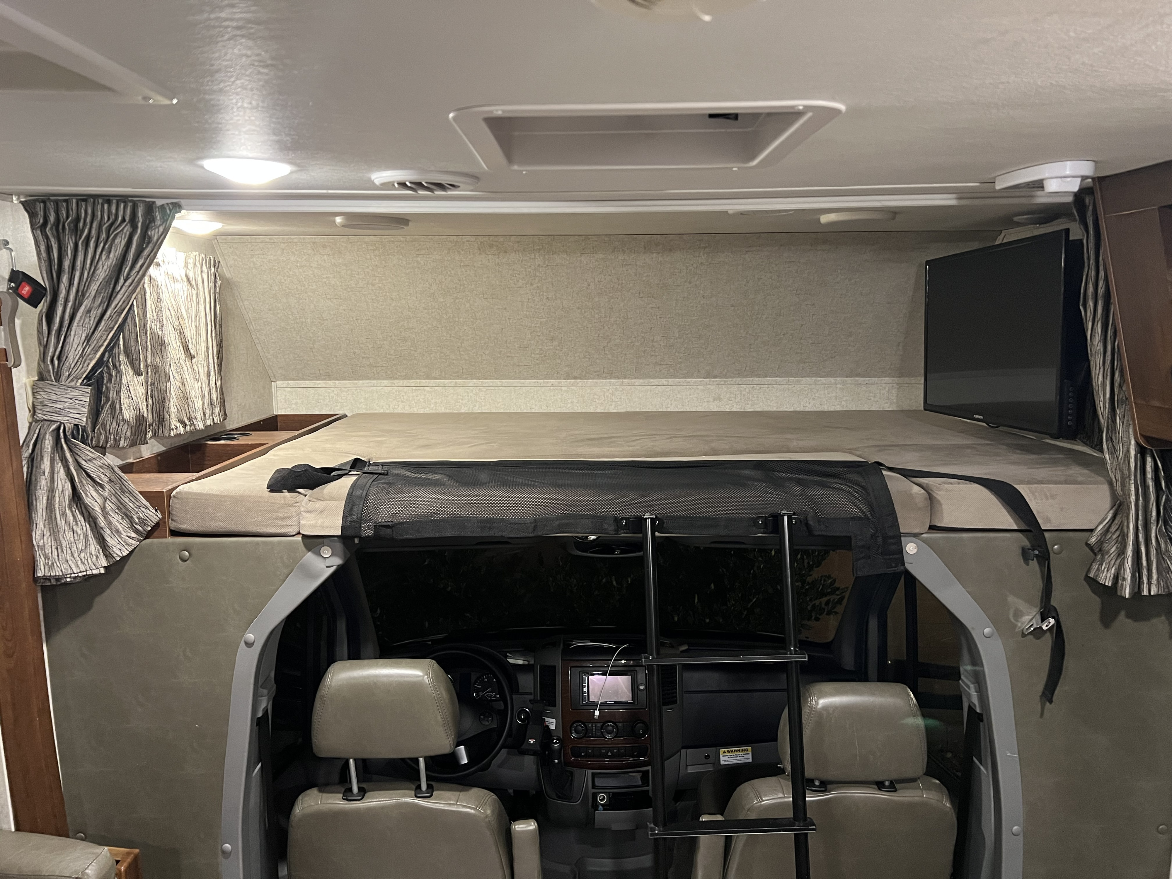 Inside a cozy RV rental. Features an over-cab bed with a safety net, access ladder, and a TV, overlooking the front cabin.. Forester MBS 2018