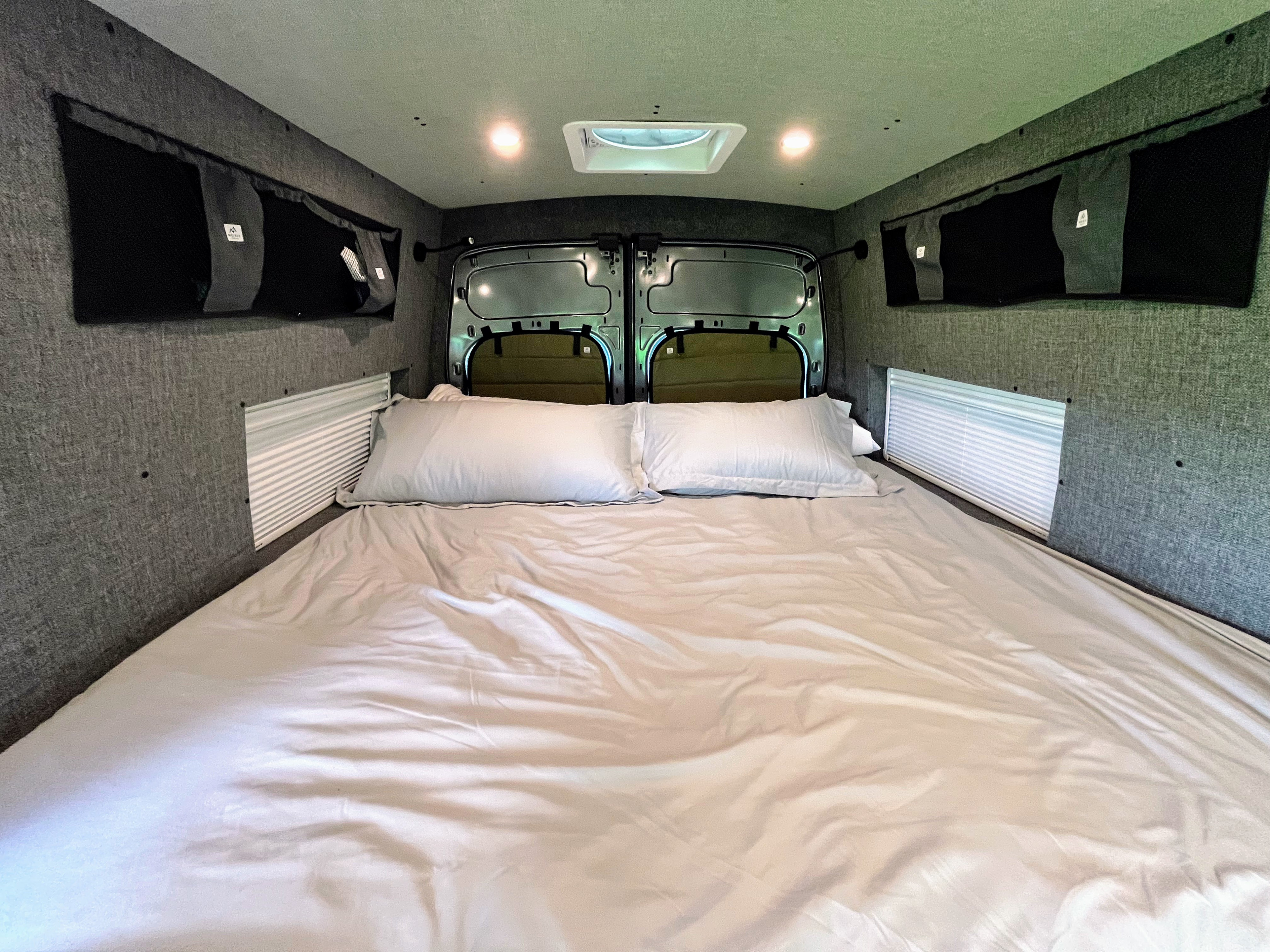 This RV rental's cozy interior features a large bed, integrated storage, and blinds for privacy.. Ford Custom Transit 2022