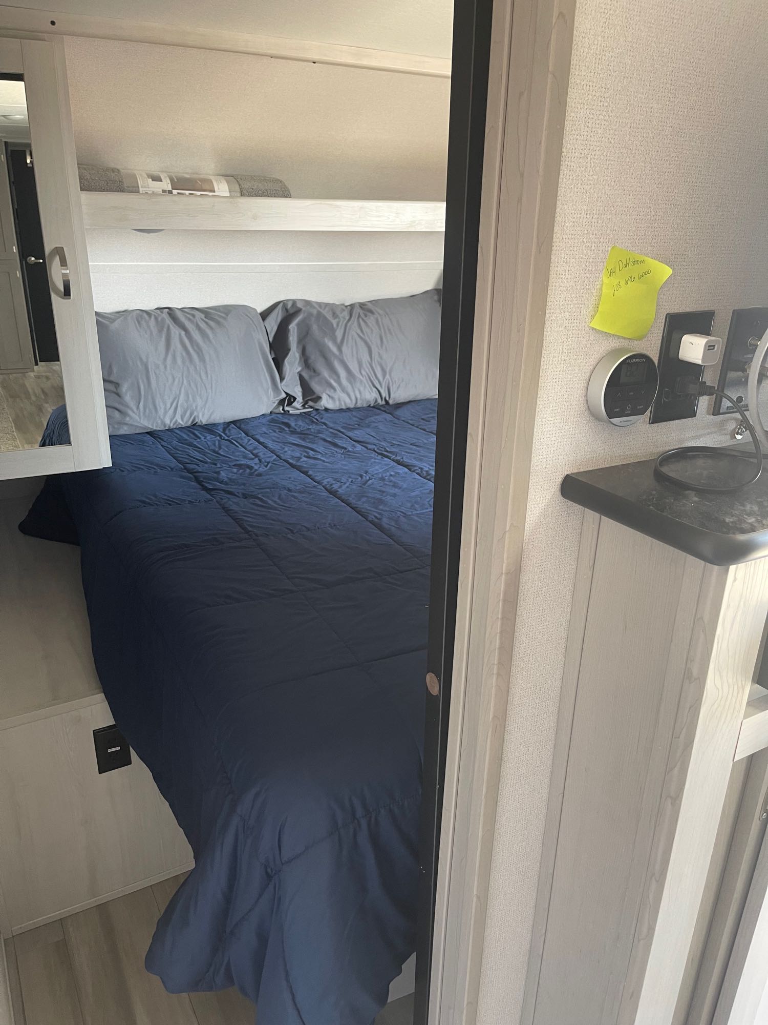 Cozy RV rental bedroom showing a bed with blue comforter, grey pillows, upper shelf, and wall-mounted controls.. Forest River Tracer 2021