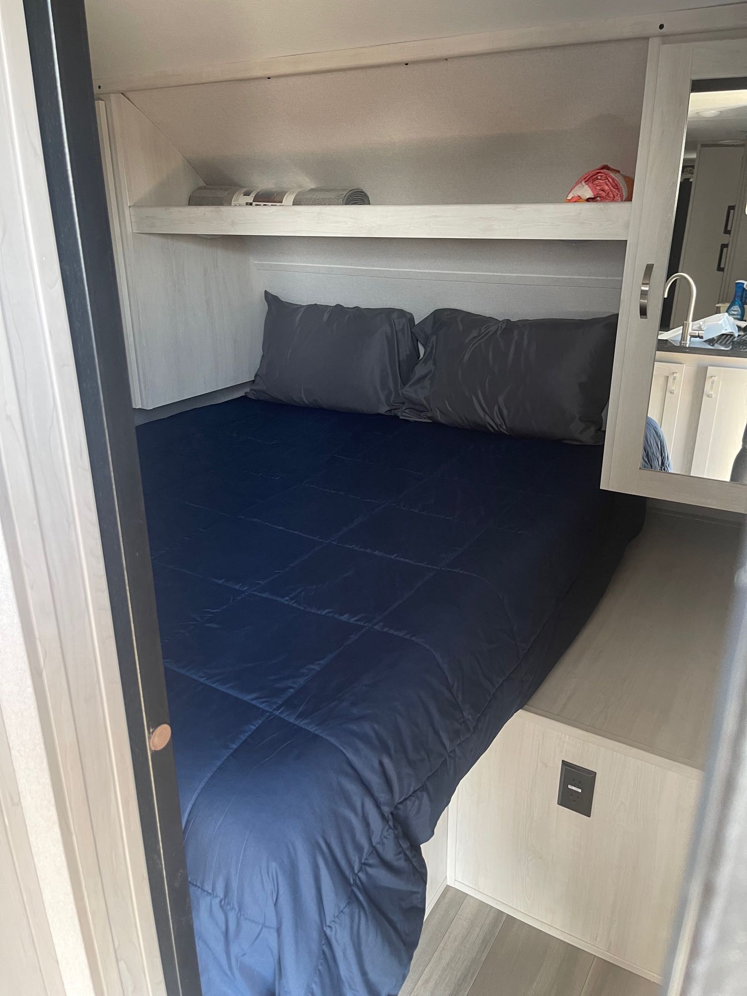 Cozy RV rental bedroom with a comfy blue bed, overhead shelf storage, and a mirrored vanity for convenient travel.. Forest River Tracer 2021