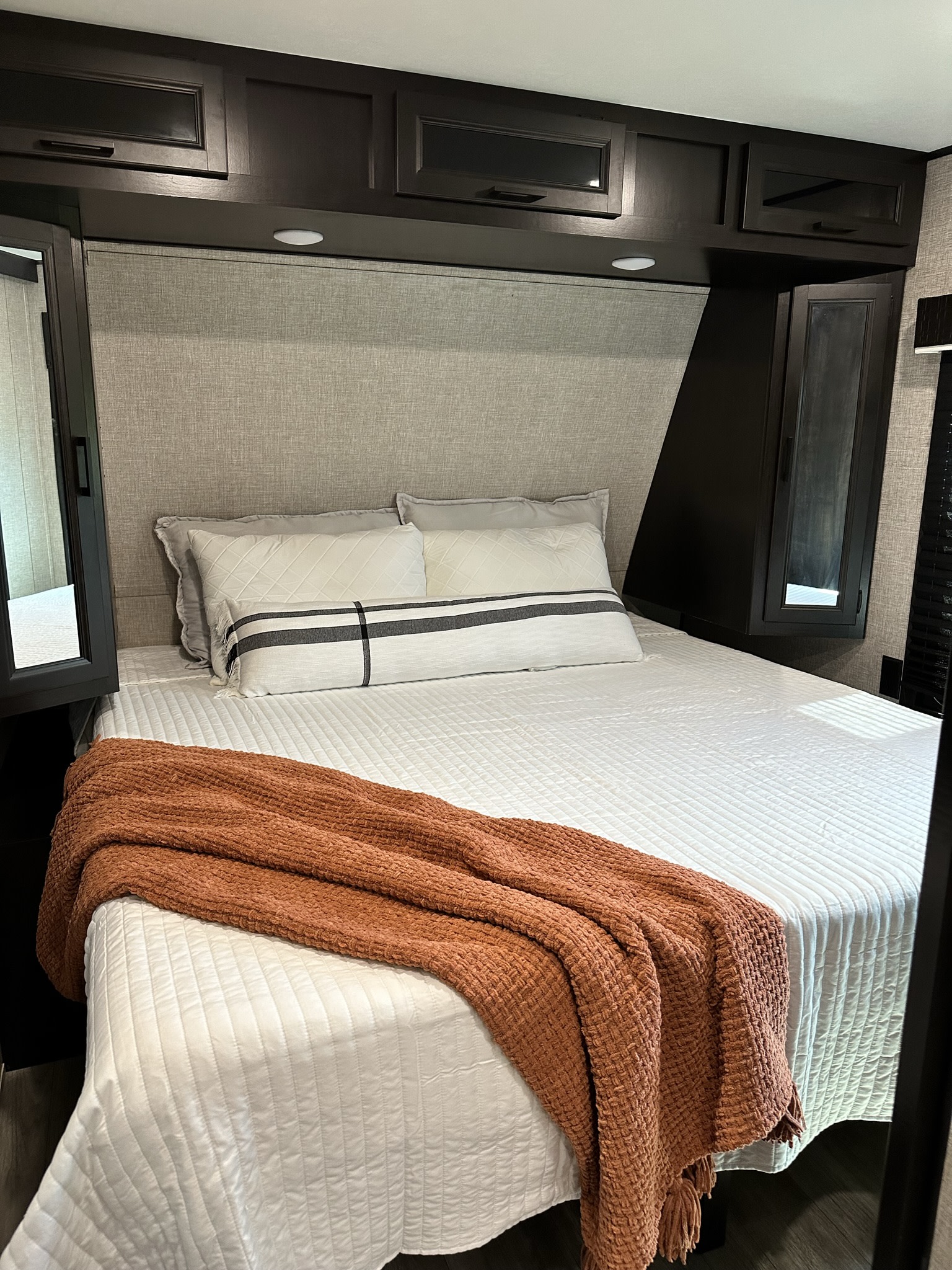 Comfortable RV rental bedroom with a white quilted bed, orange throw blanket, and dark wood storage above.. Jayco Jay Flight 2022