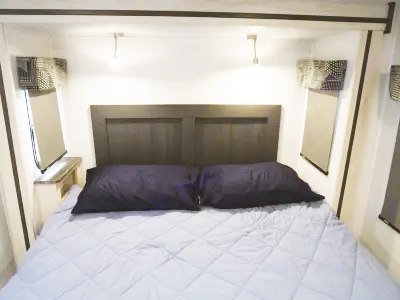 Cozy RV rental bedroom featuring a dark headboard, light blue bedding, and two dark pillows. Ideal for your next road trip.. Forest River Sunseeker Classic 2023