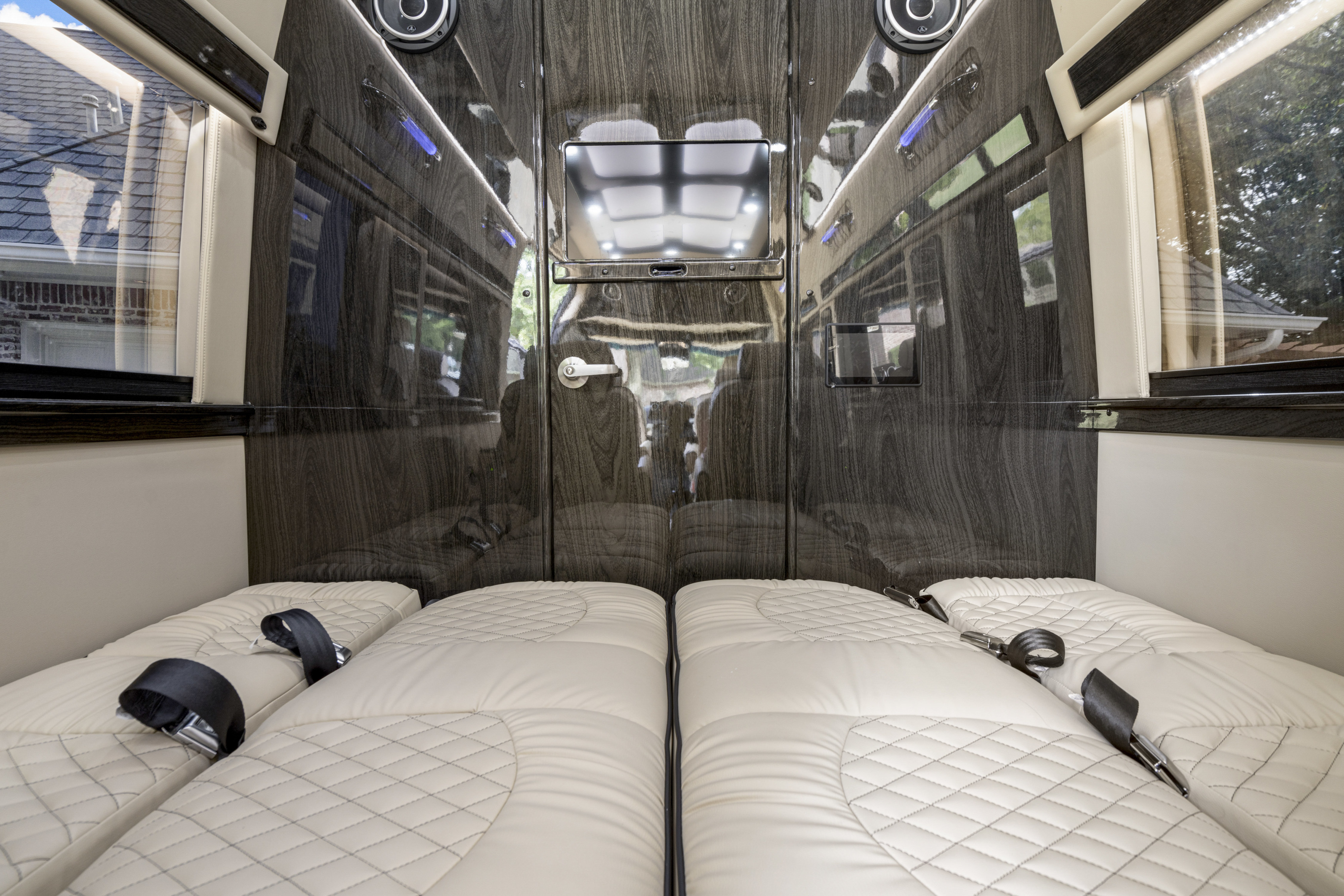 Luxury RV rental: plush quilted beds with seatbelts, glossy wood walls, windows, and central TV offer travel comfort.. Ultimate Toys Ultimate Coach 2024