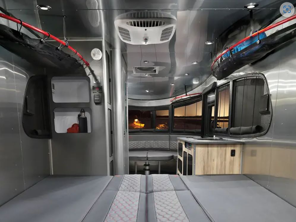 Explore this modern RV rental interior. Features a convertible bed, dining area, and compact kitchen. Sleek silver walls.. Airstream Basecamp 2023