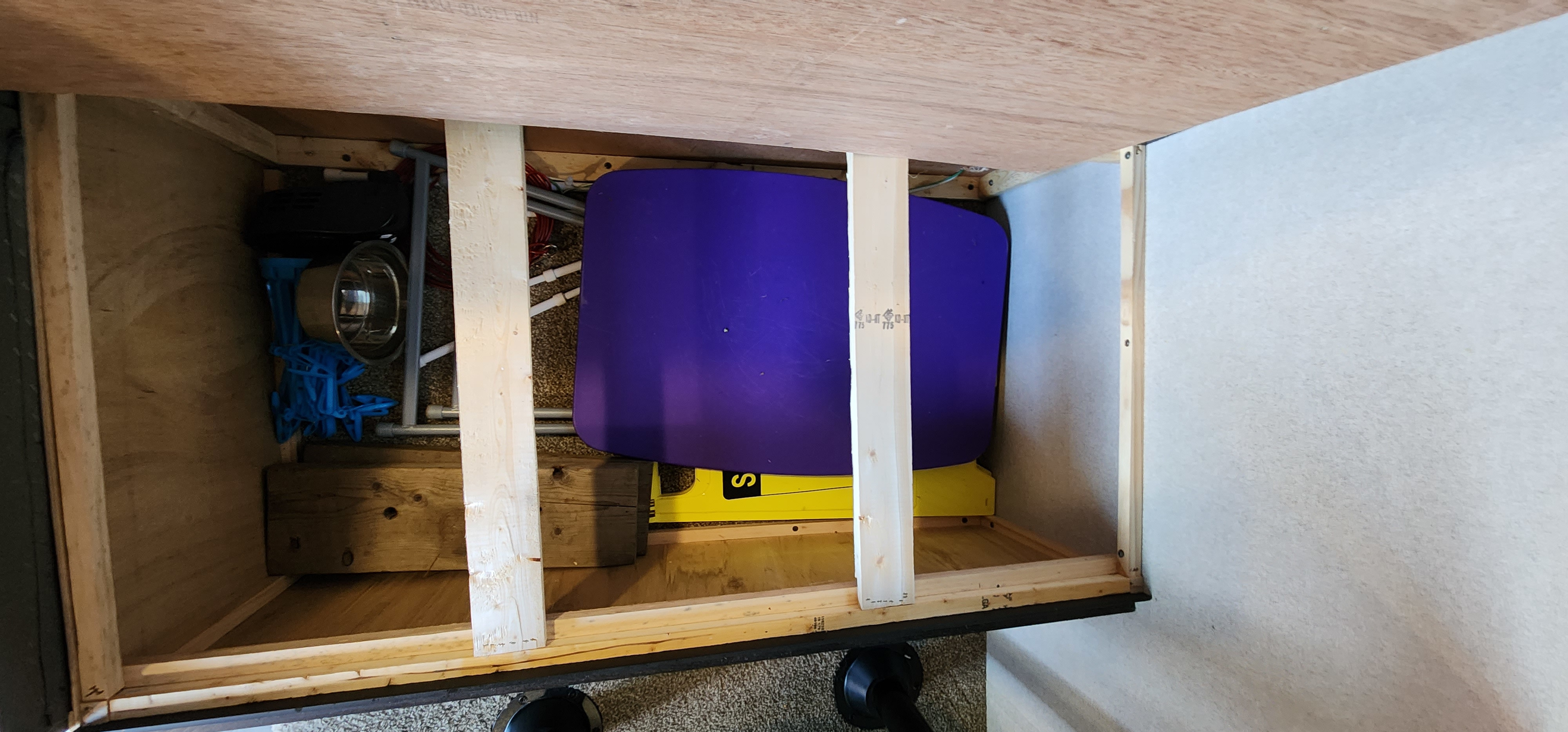 RV rental: Under-bed storage with a purple water tank, pet bowl, and blue items, set within wooden framing.. Keystone RV Summerland Mini 2019