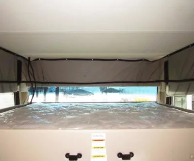 RV rental sleeping area: a comfortable bunk with mattress, pop-up fabric walls, and bright outdoor views.. Thor Miramar 2022